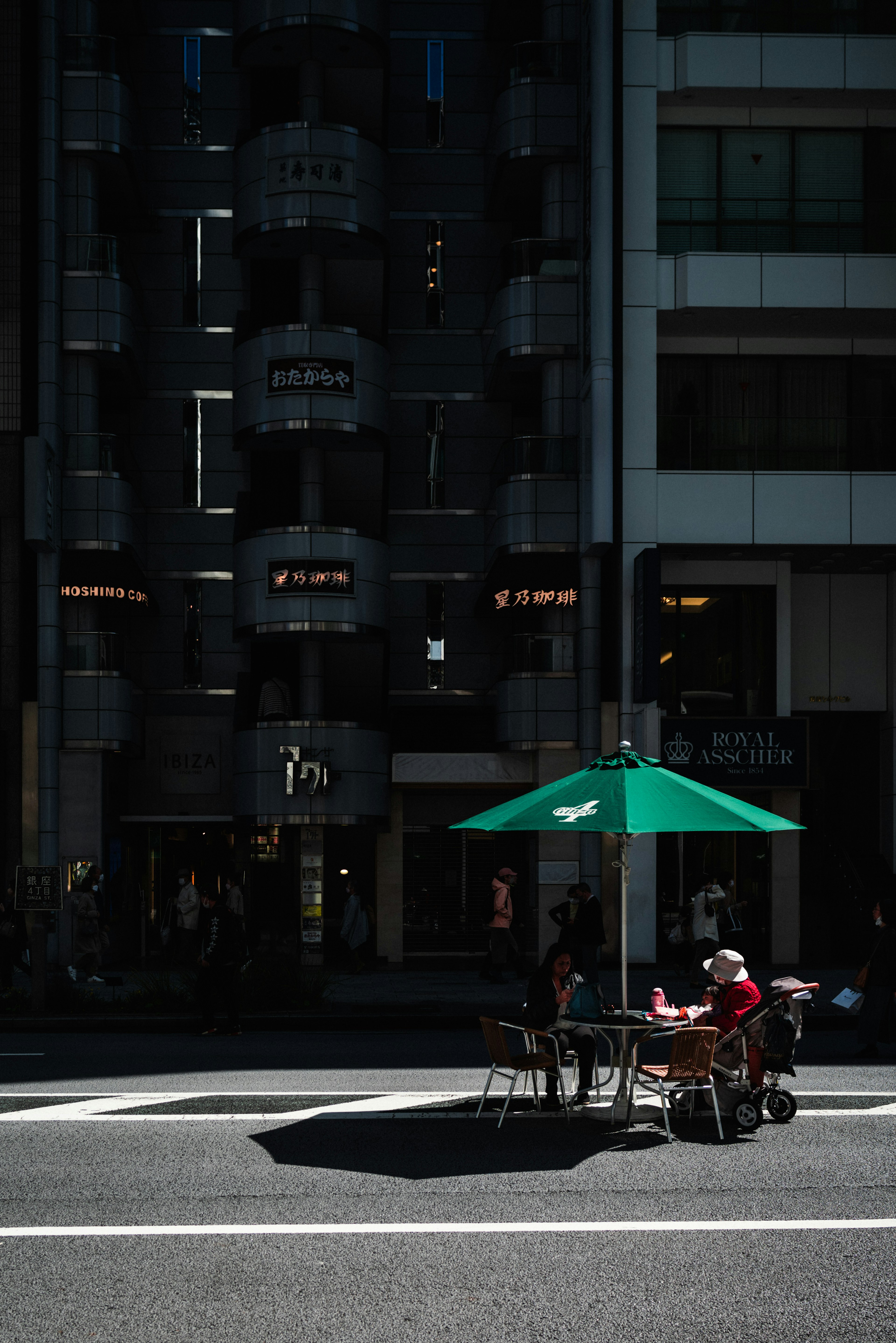 Two people sitting at a table under a green umbrella with a dark building in the background