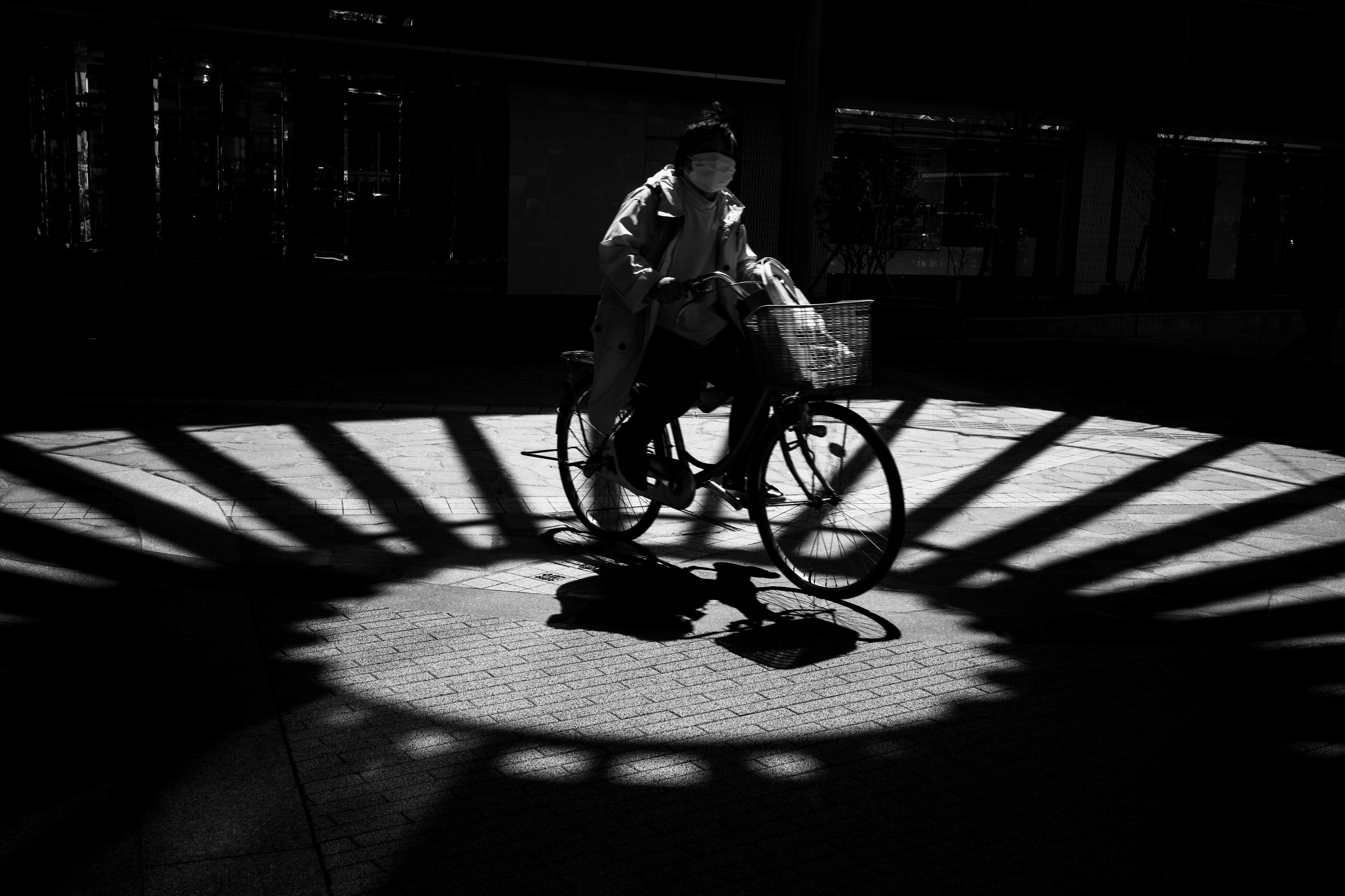 自転車に乗る人物と影の模様が印象的なモノクロ写真