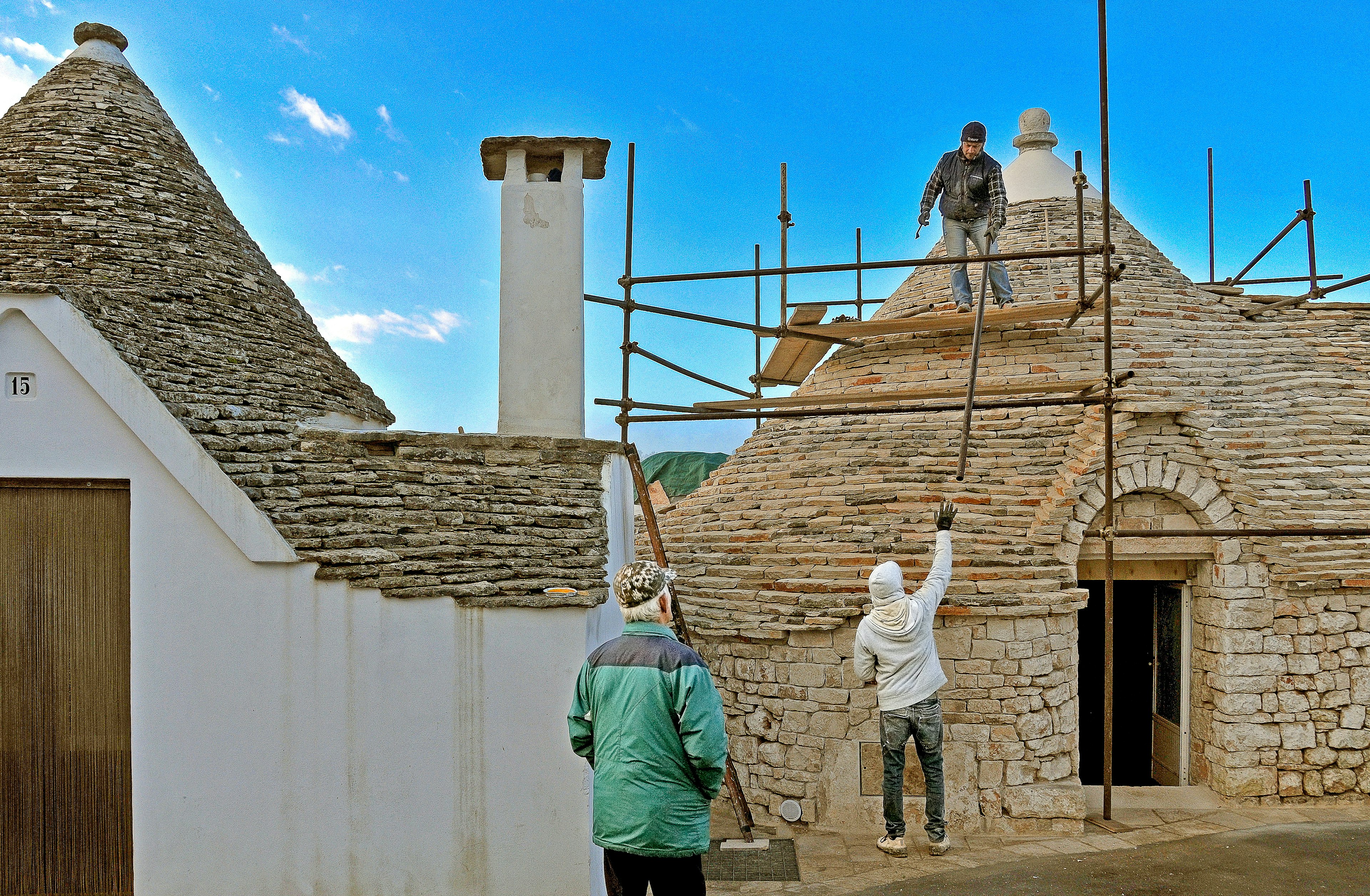 Men working on the roof of a trullo building with scaffolding