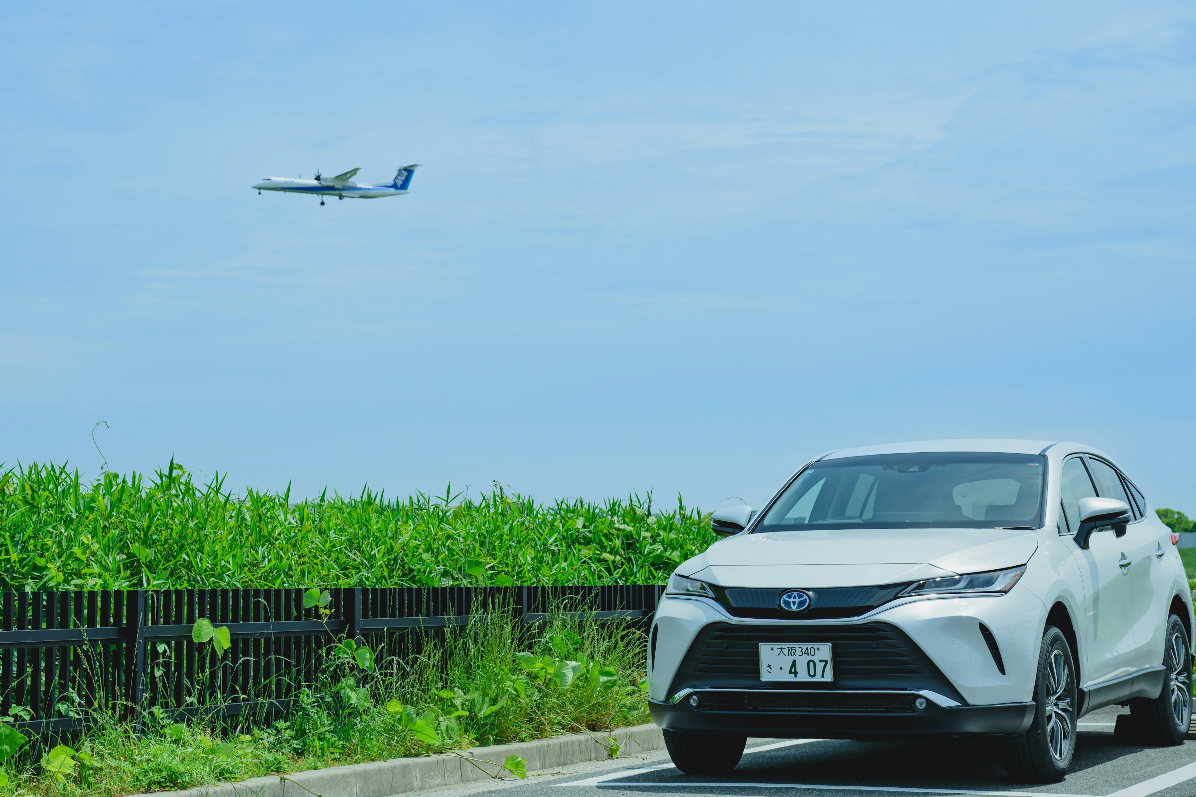 Ein weißes Auto am Straßenrand mit einem Flugzeug, das am blauen Himmel fliegt