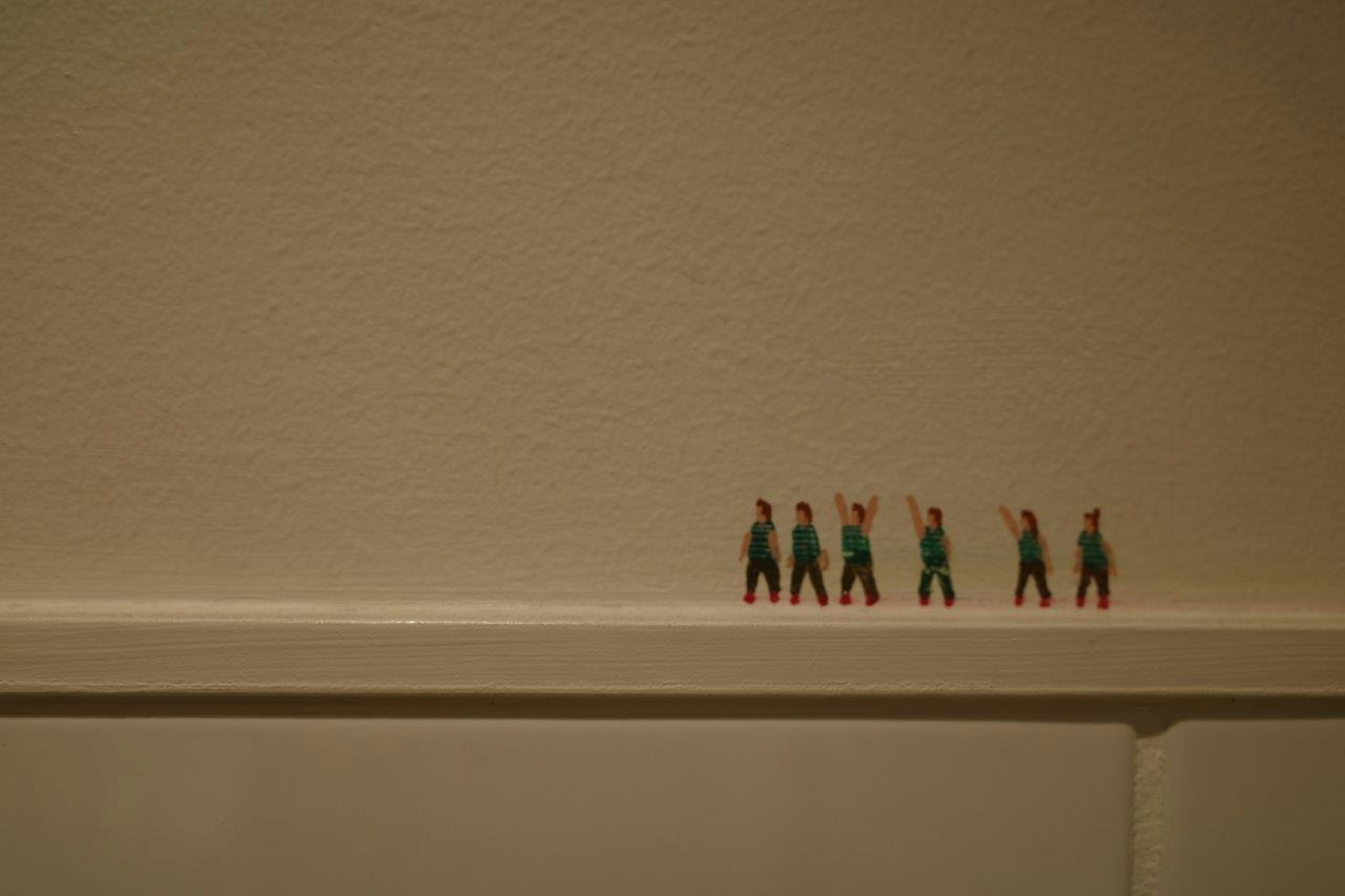 Petites figurines vertes debout sur un rebord contre un mur uni