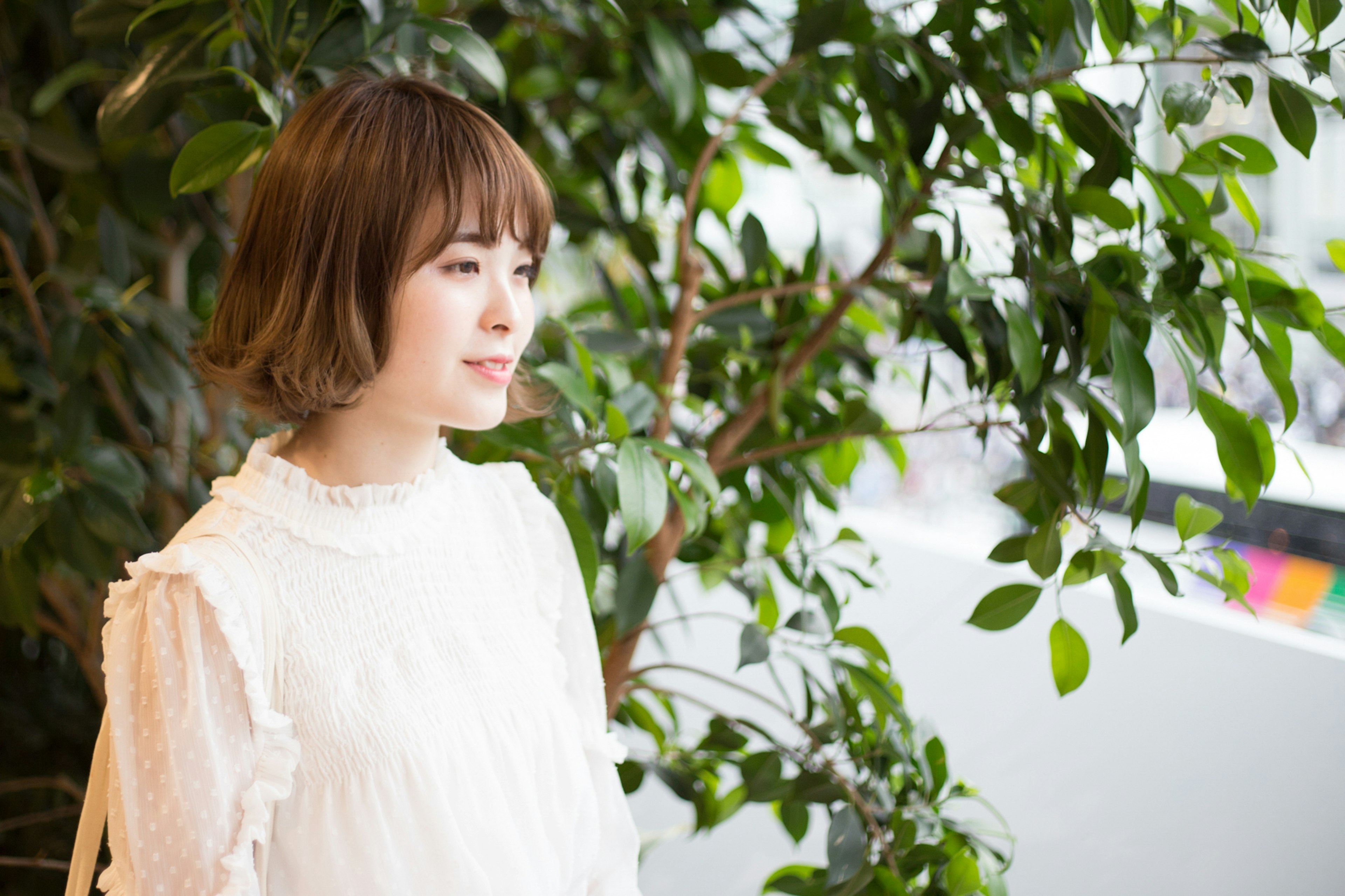 Portrait of a woman standing in front of green plants wearing a white blouse