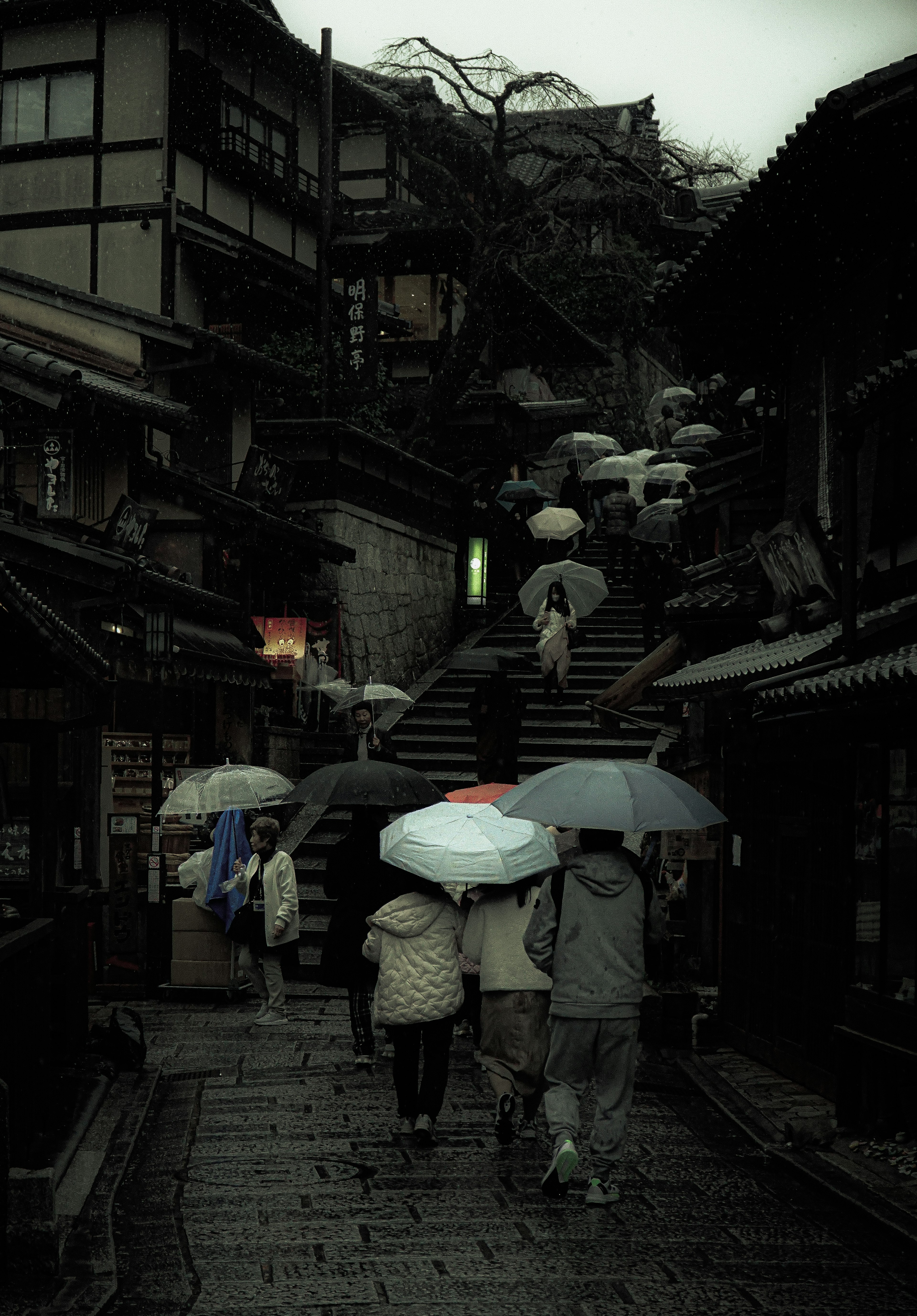 雨の日の古い街並みに傘をさした人々が階段を上る風景