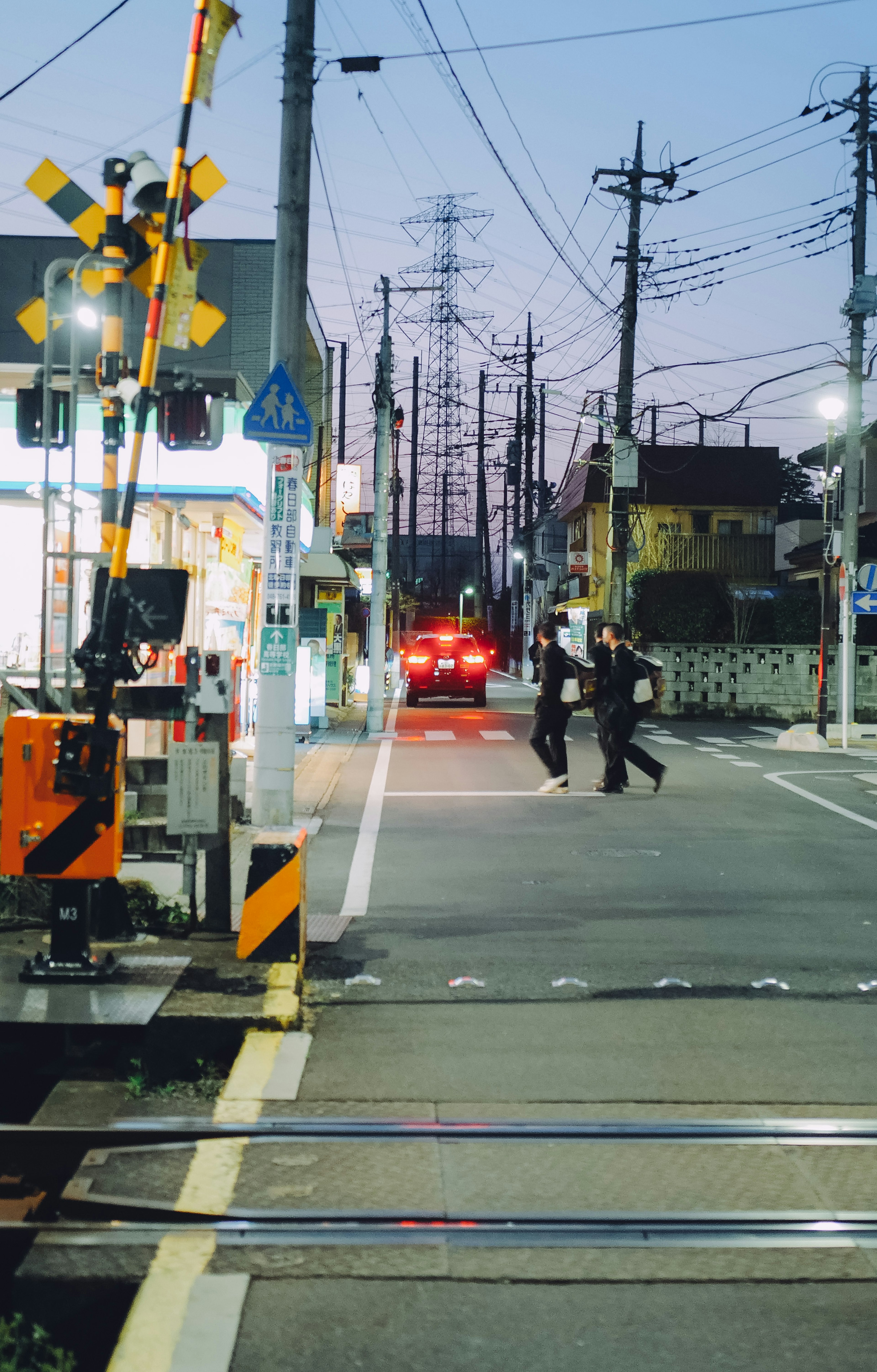 Pedestrians crossing the street at dusk near a railway crossing