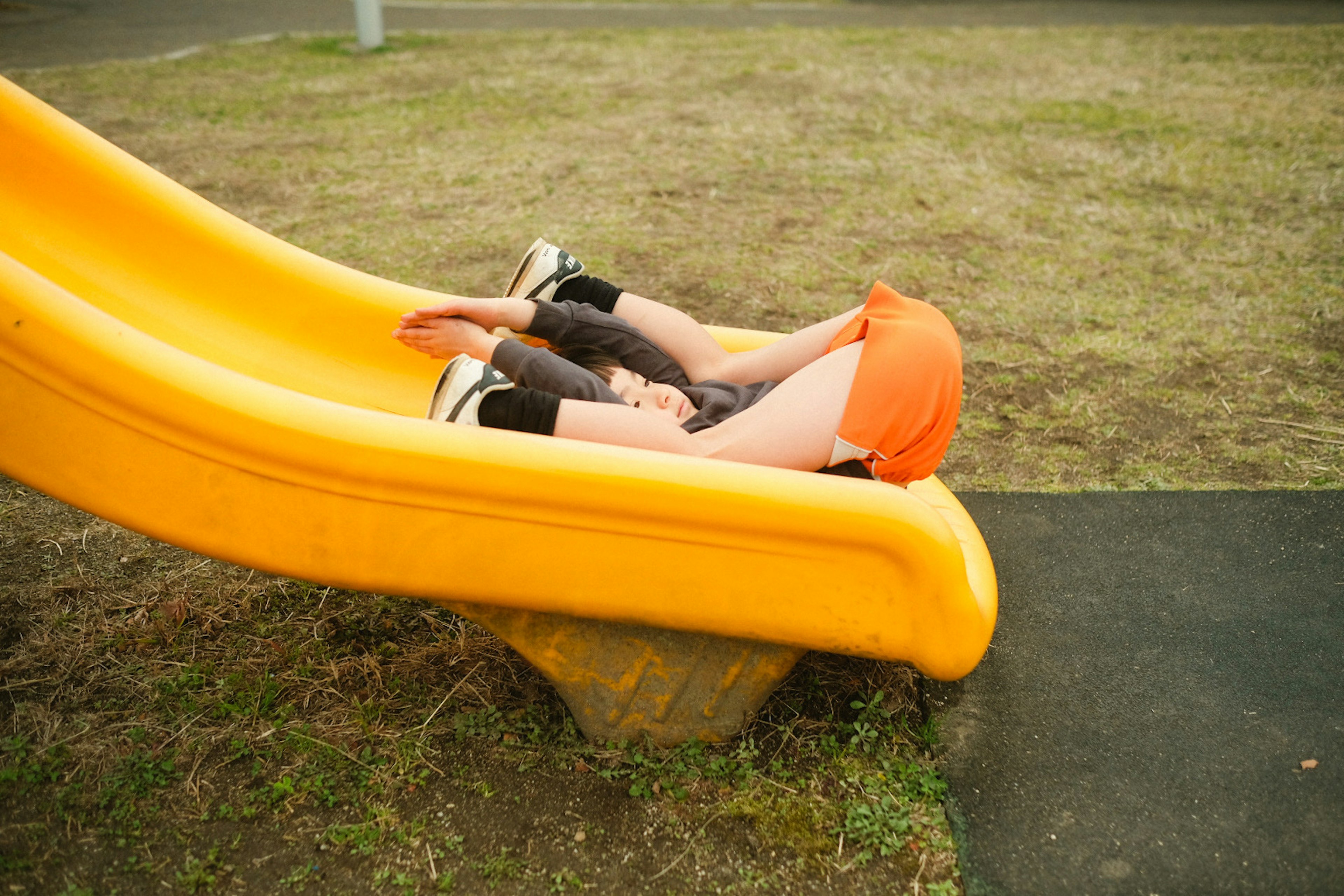 Enfant allongé sur un toboggan jaune portant un short orange vif