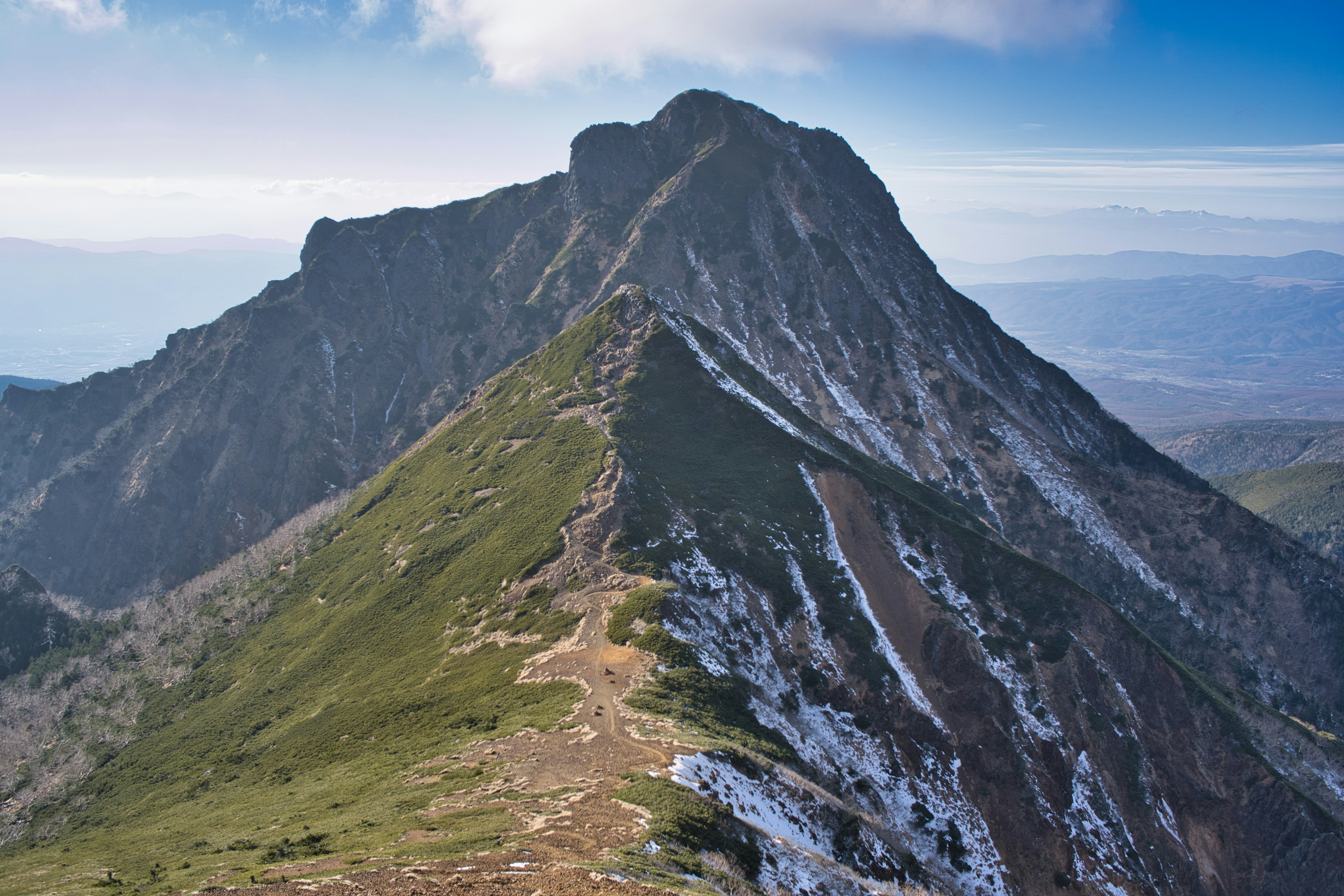 Paysage montagneux magnifique avec des pentes verdoyantes et un sommet enneigé sous un ciel bleu avec des nuages blancs