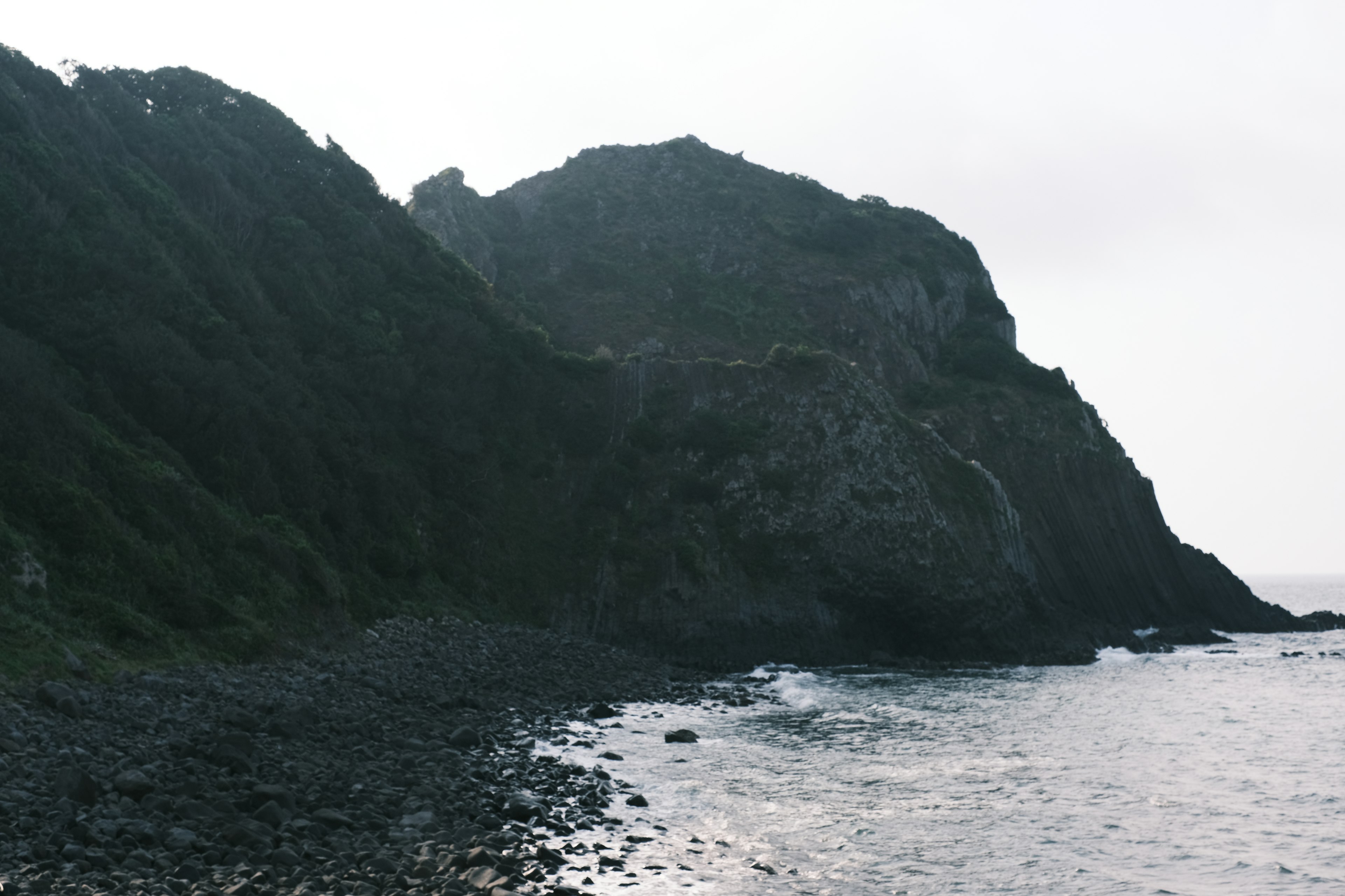 Pemandangan pesisir dengan tebing berbatu dan gunung berkabut