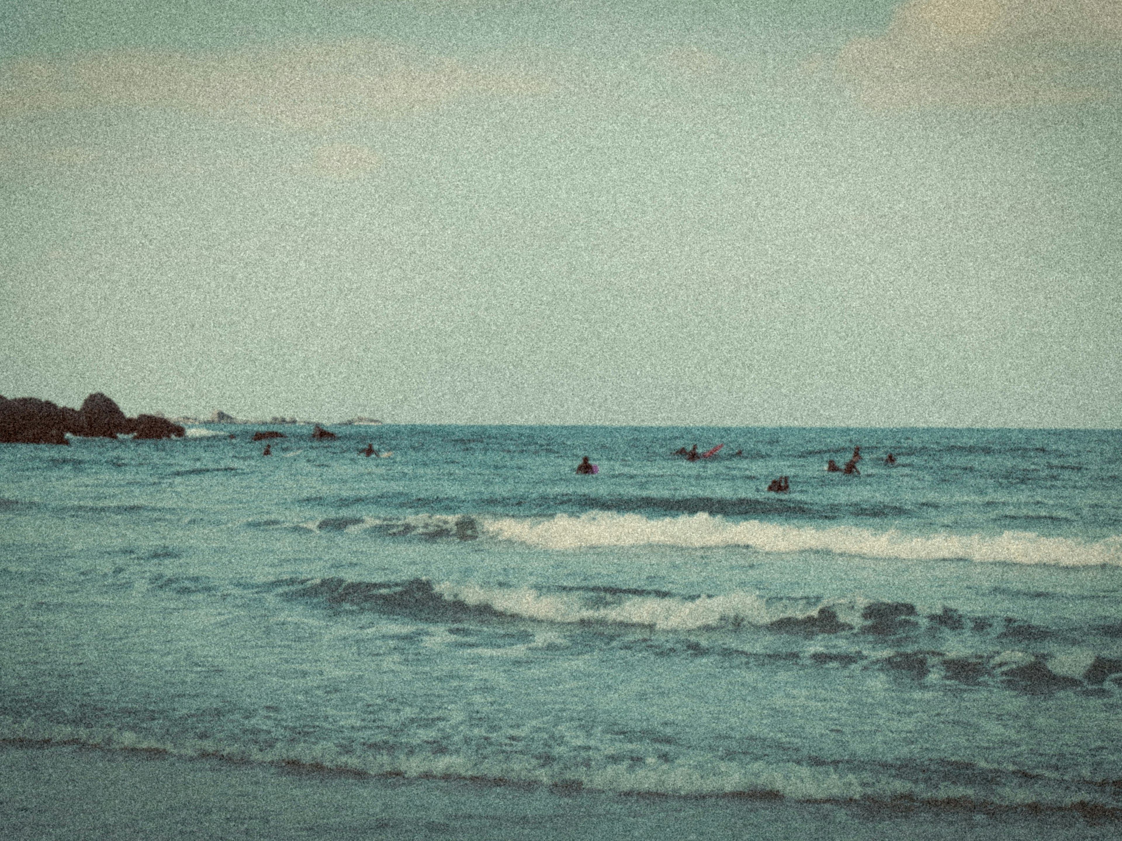 Pemandangan pantai yang tenang dengan siluet orang bermain di lautan