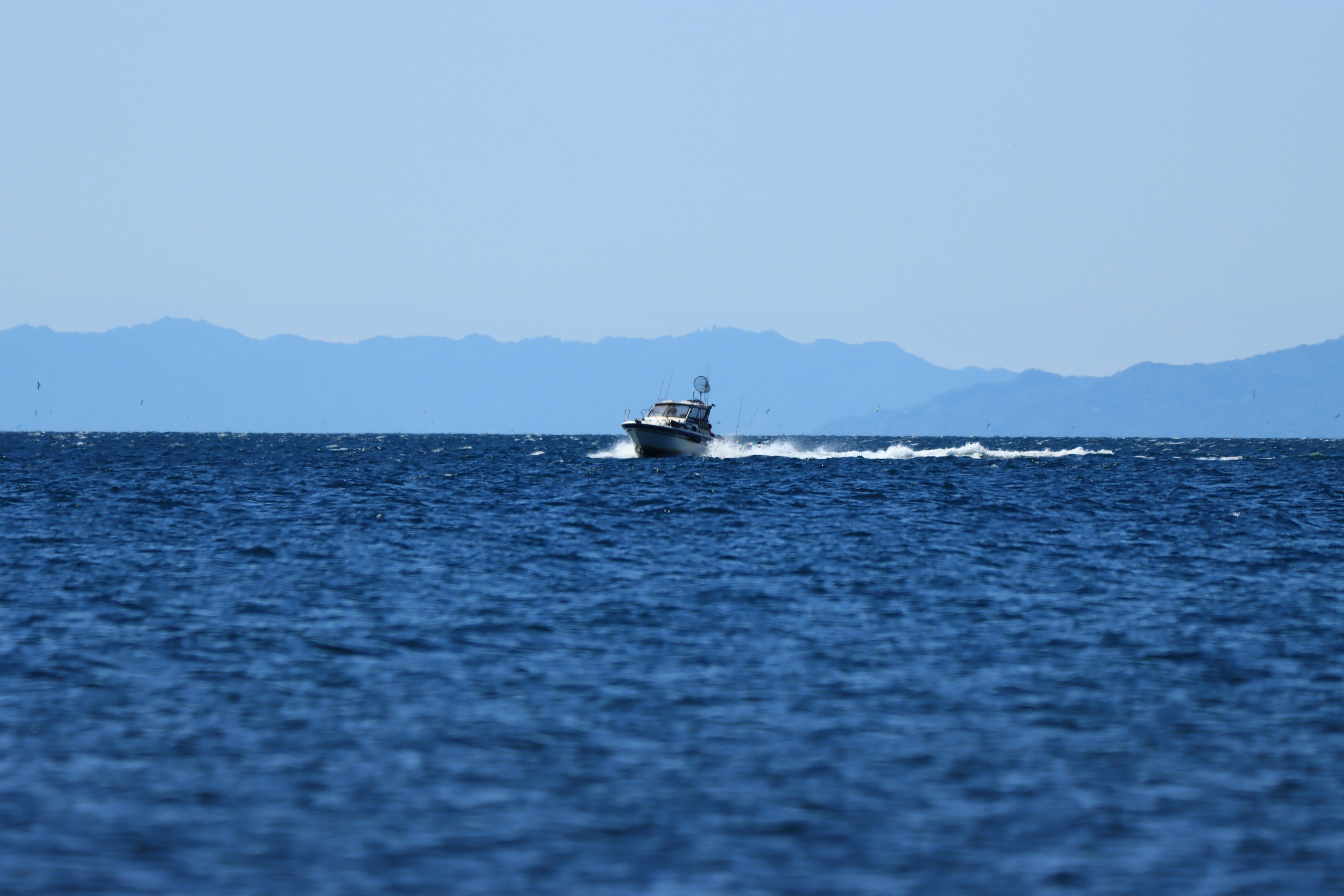 A small boat navigating on a blue sea with distant mountains in the background