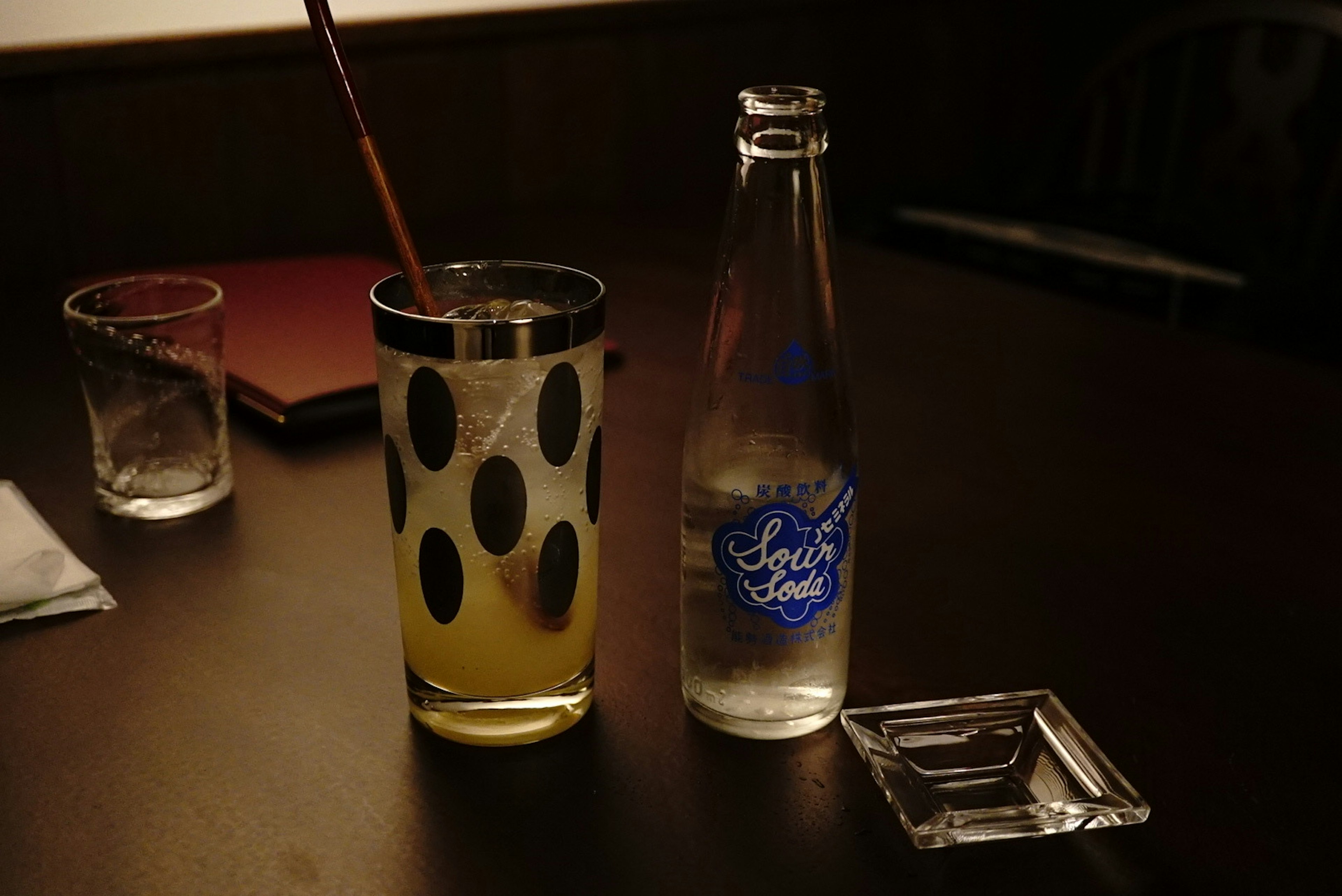 A polka-dotted glass containing an orange drink alongside a clear bottle of water on a table