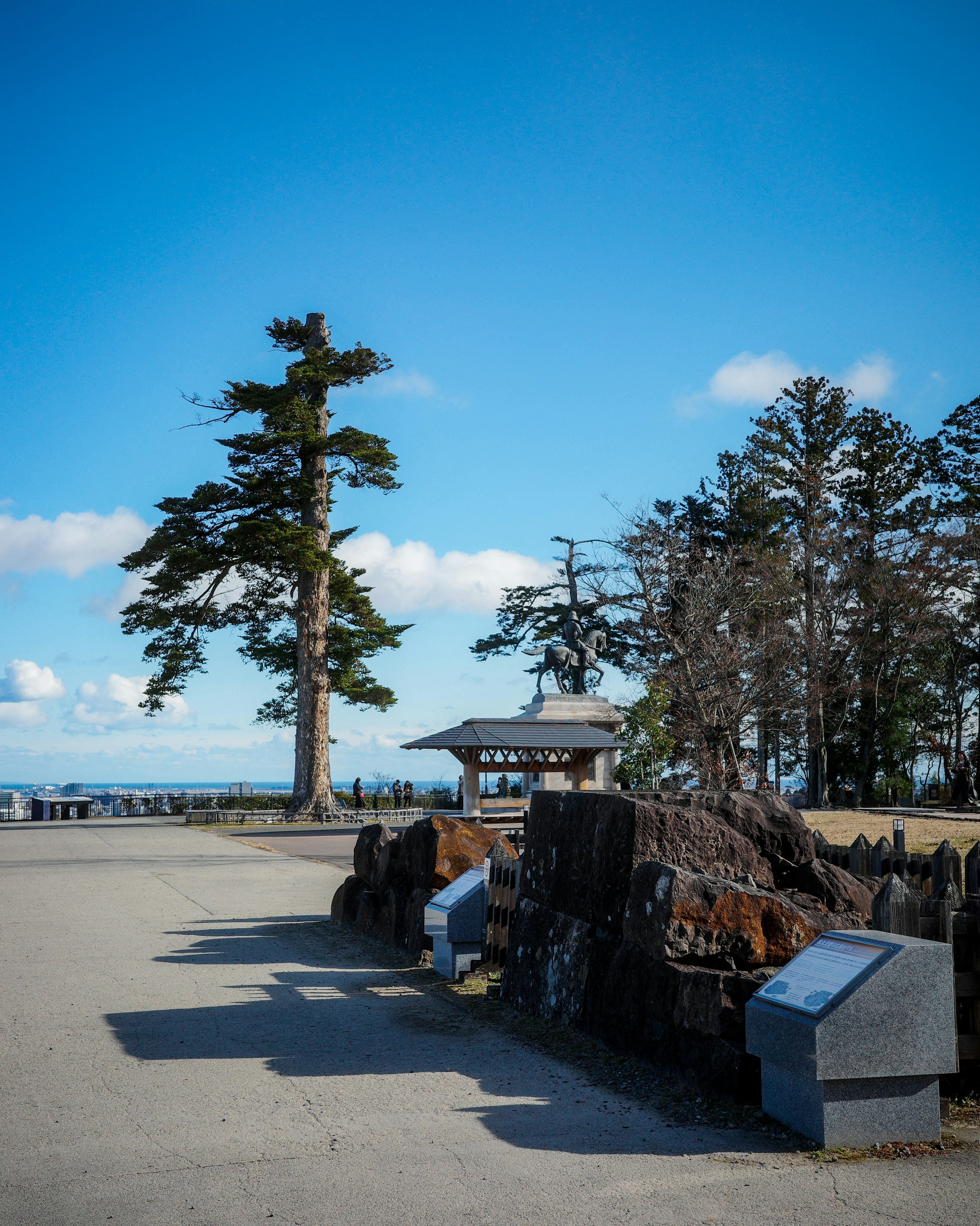 青空の下にある大きな木と石碑が見える公園の風景