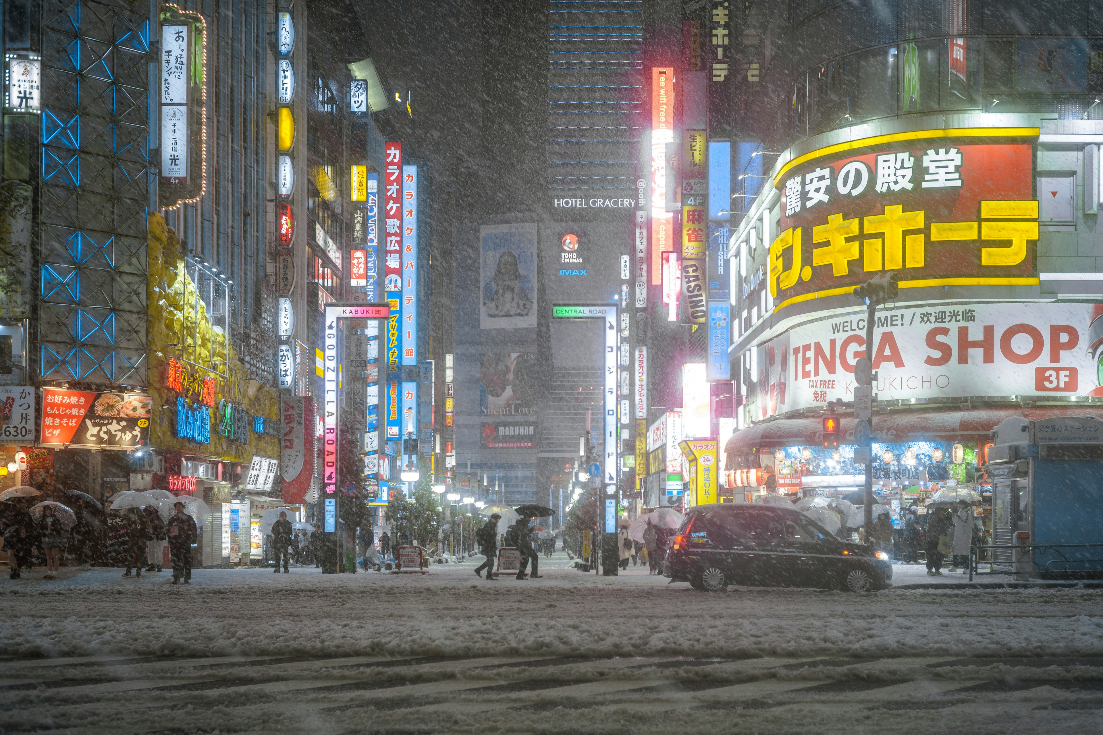 Jalan bersalju di Shinjuku di malam hari dengan lampu neon yang cerah dan pejalan kaki