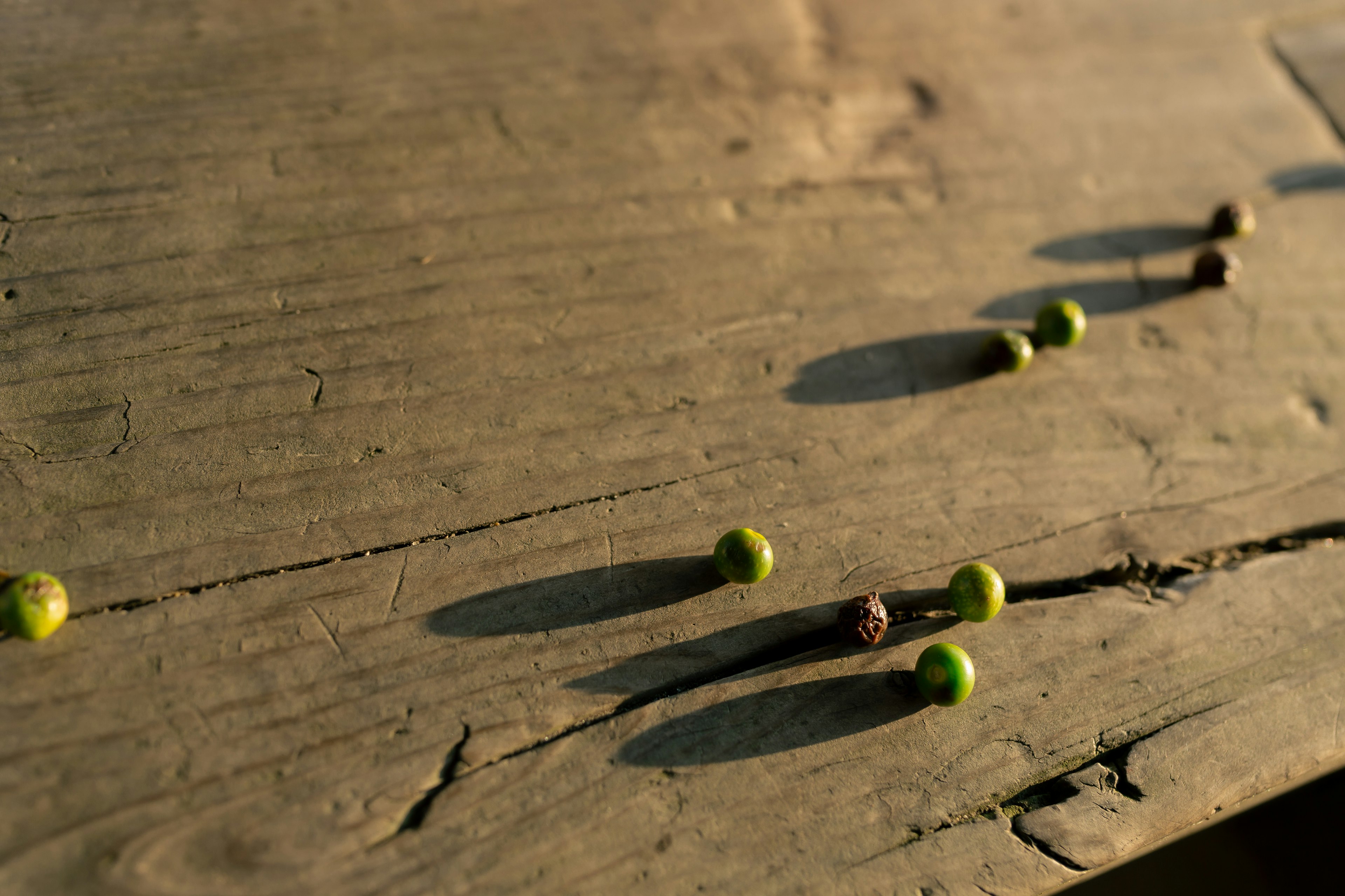 Small green and brown spheres casting shadows on a wooden table