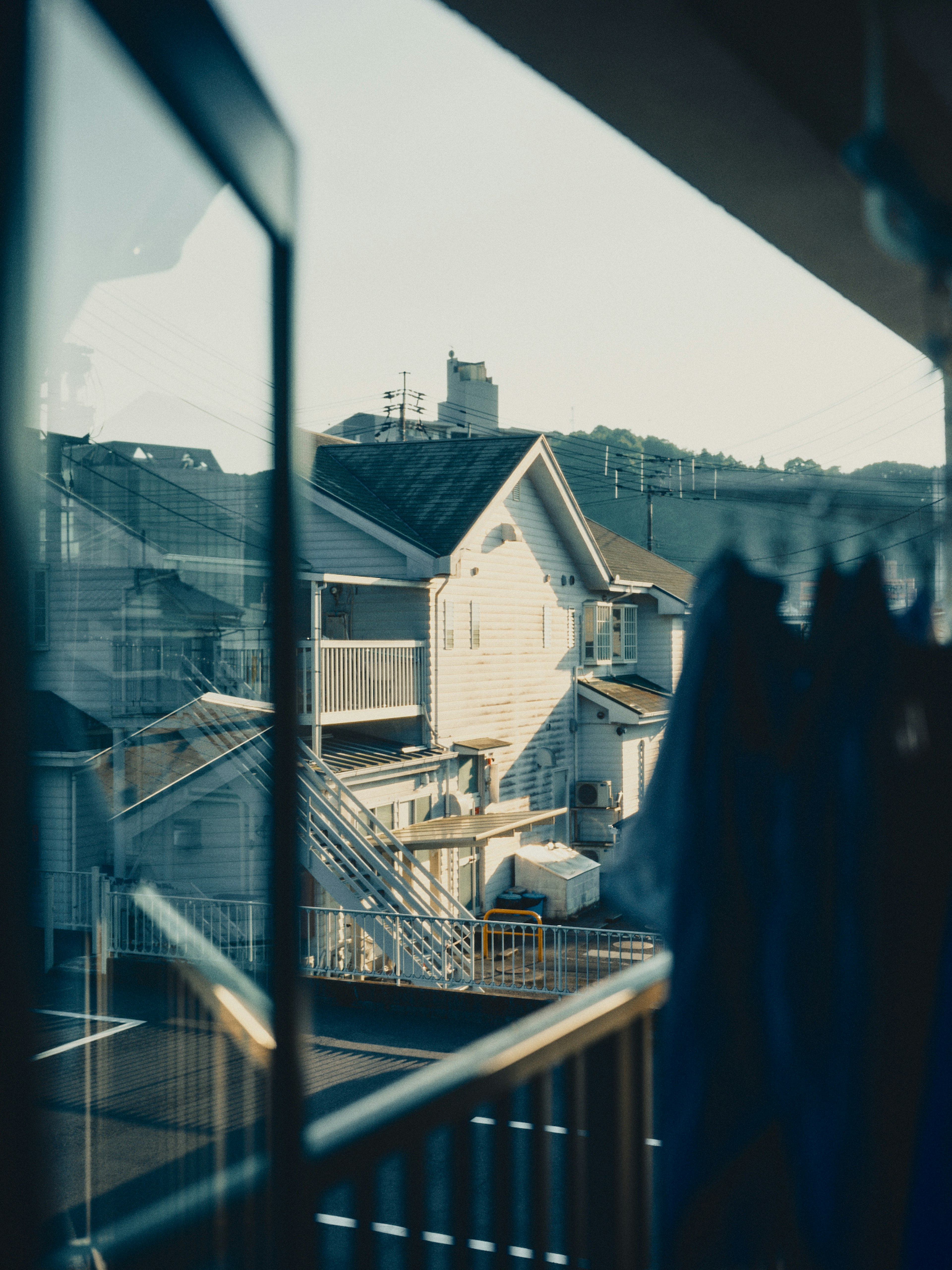 Blick auf ein japanisches Wohngebiet durch ein Fenster mit hängenden blauen Kleidungsstücken