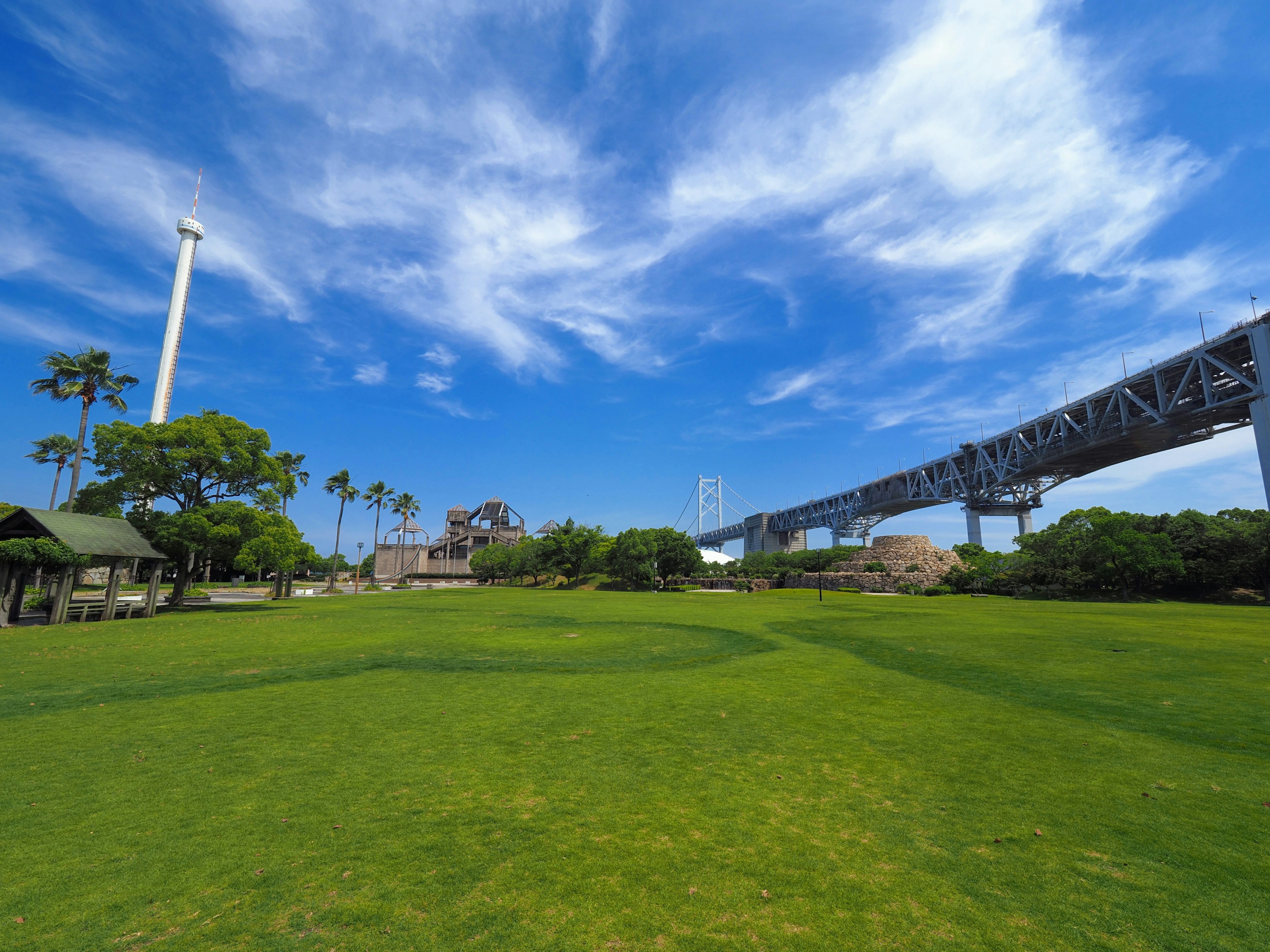 Parque verde bajo un cielo azul con nubes blancas y un puente elevado