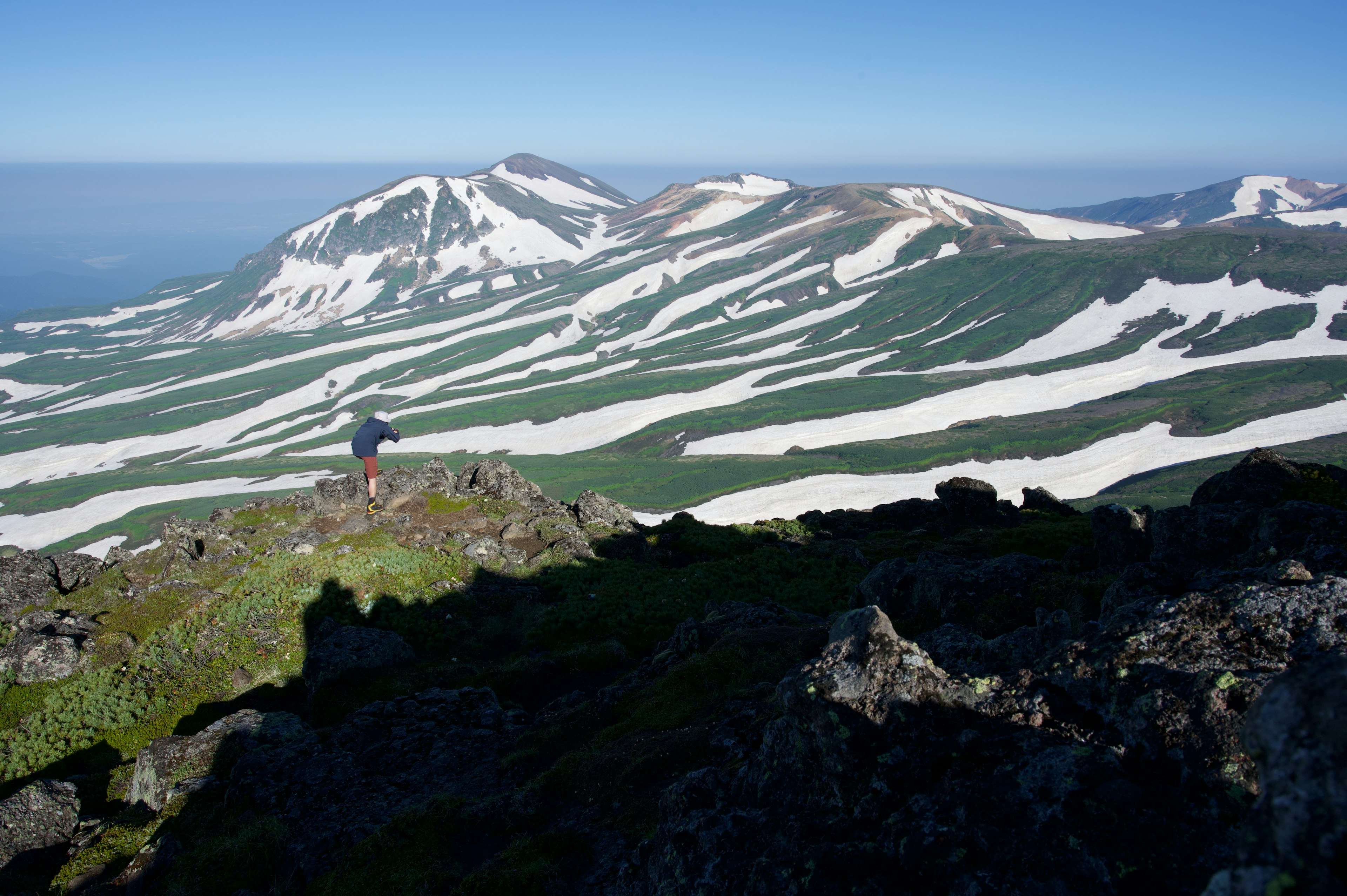 Hiker overlooking snow-capped mountains and green terrain