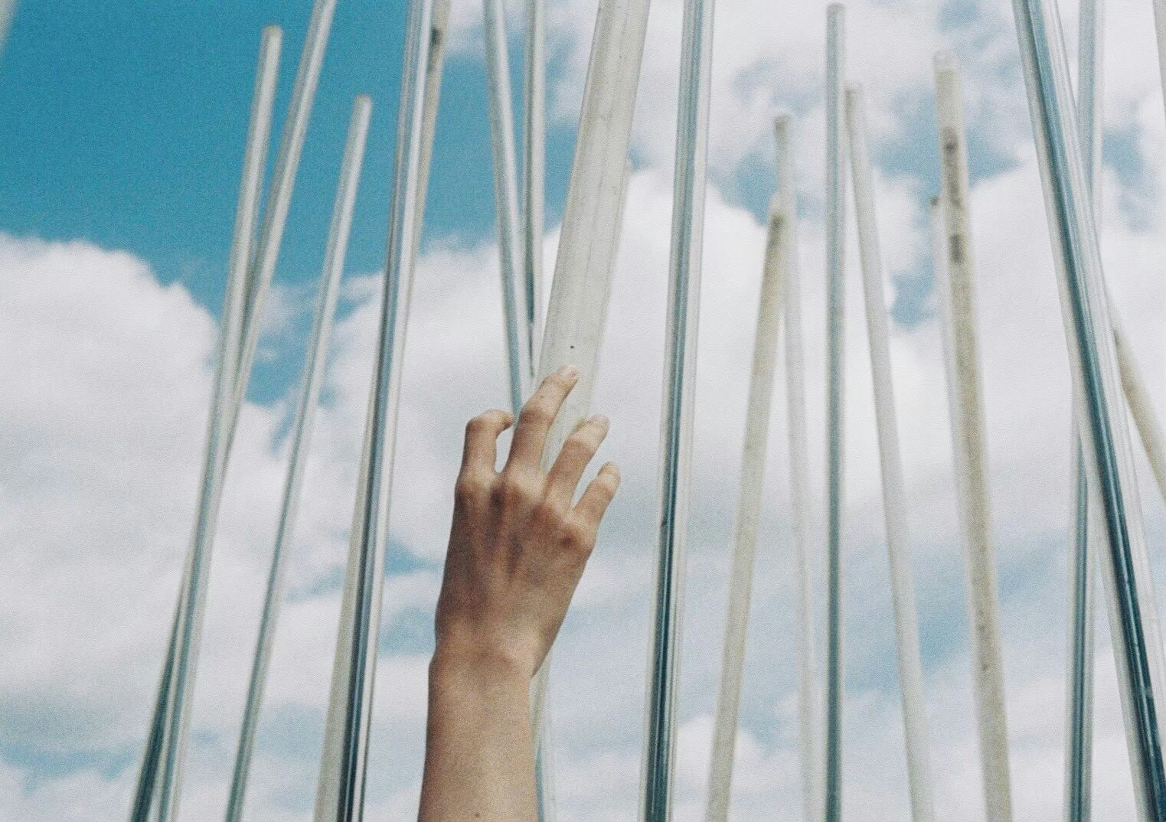 Mano alcanzando varillas transparentes contra un cielo azul