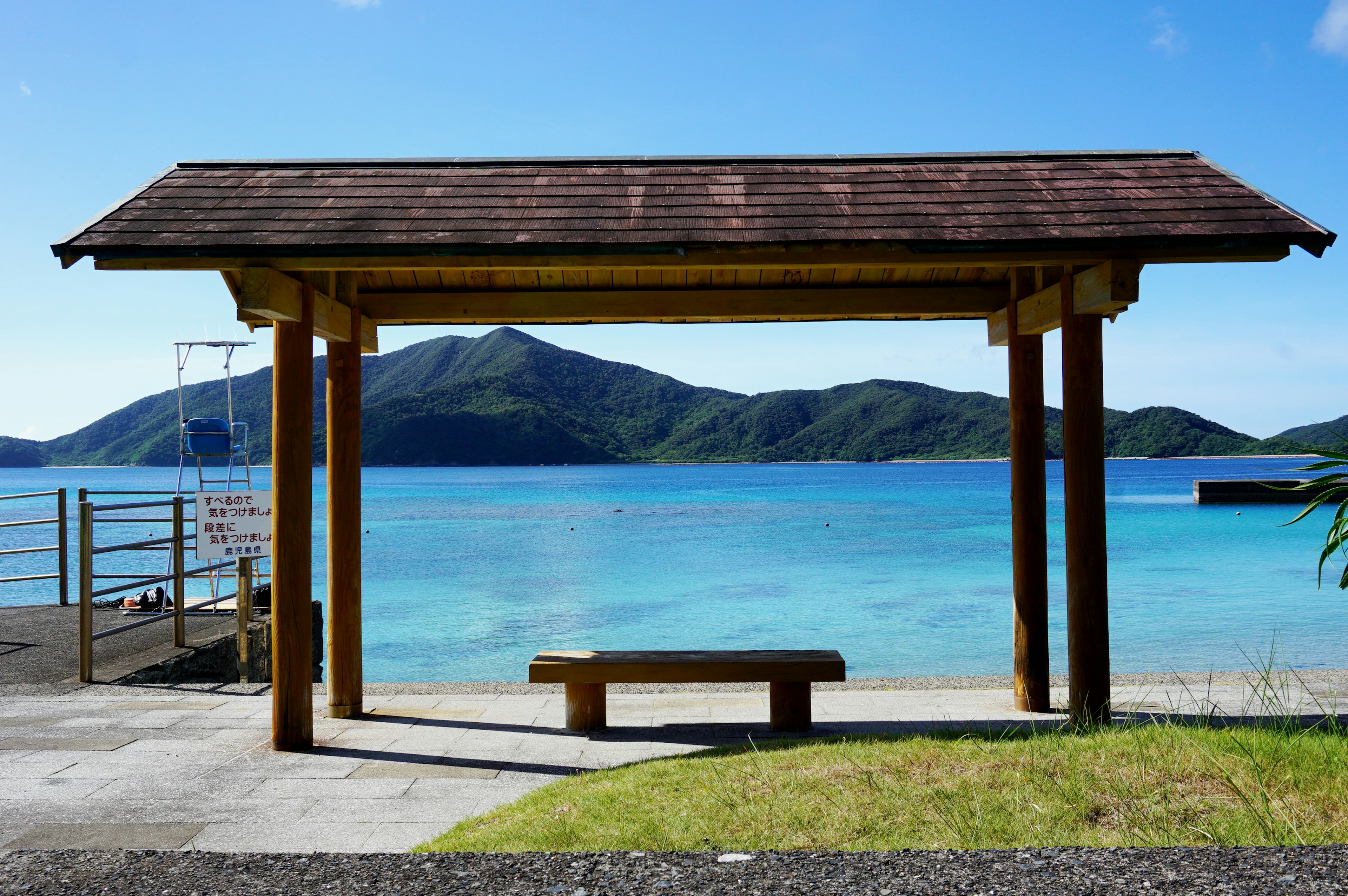 Pavillon de plage avec banc en bois surplombant la mer bleue et les montagnes