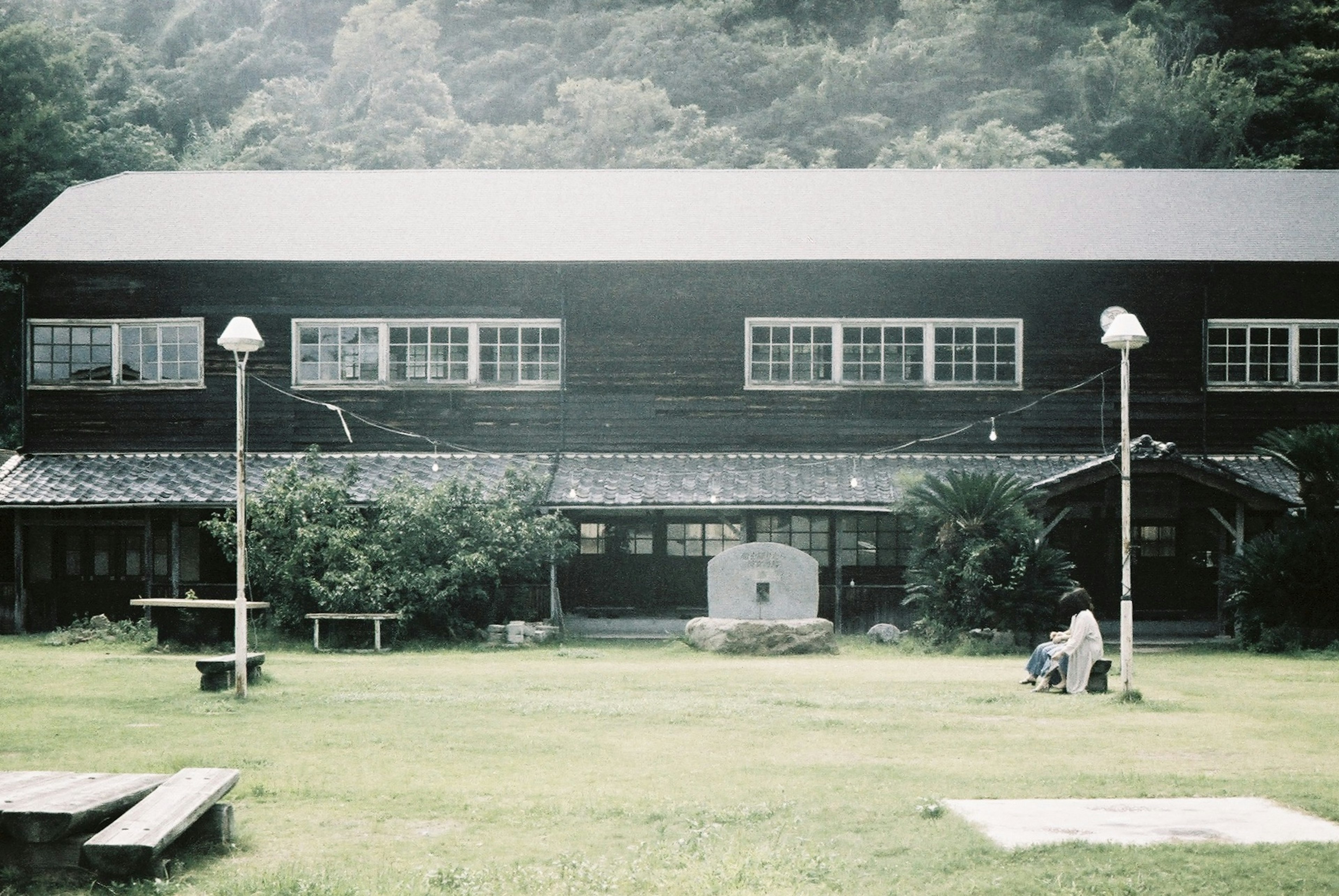 緑に囲まれた古い木造の建物とベンチがある風景