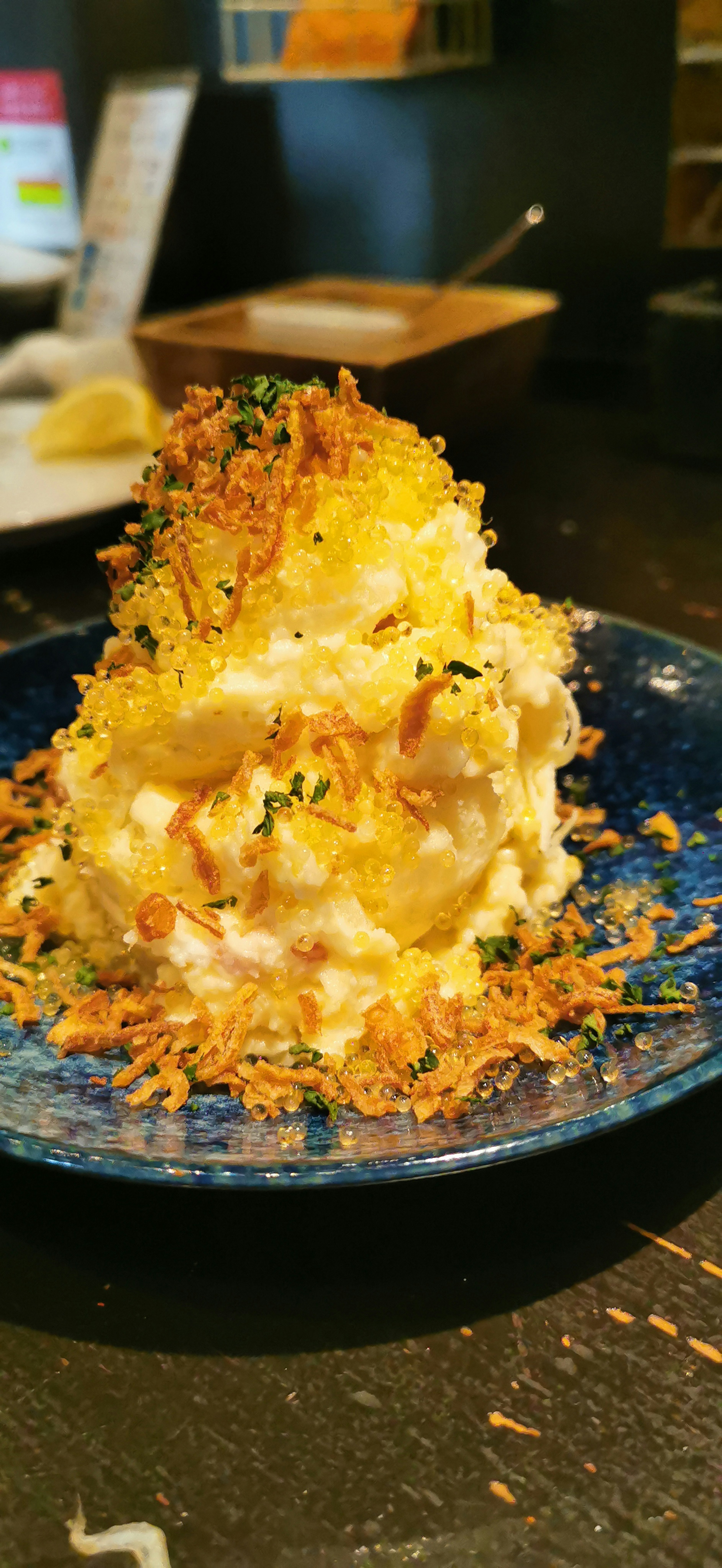 Creamy potato salad piled high on a blue plate topped with crispy garnish