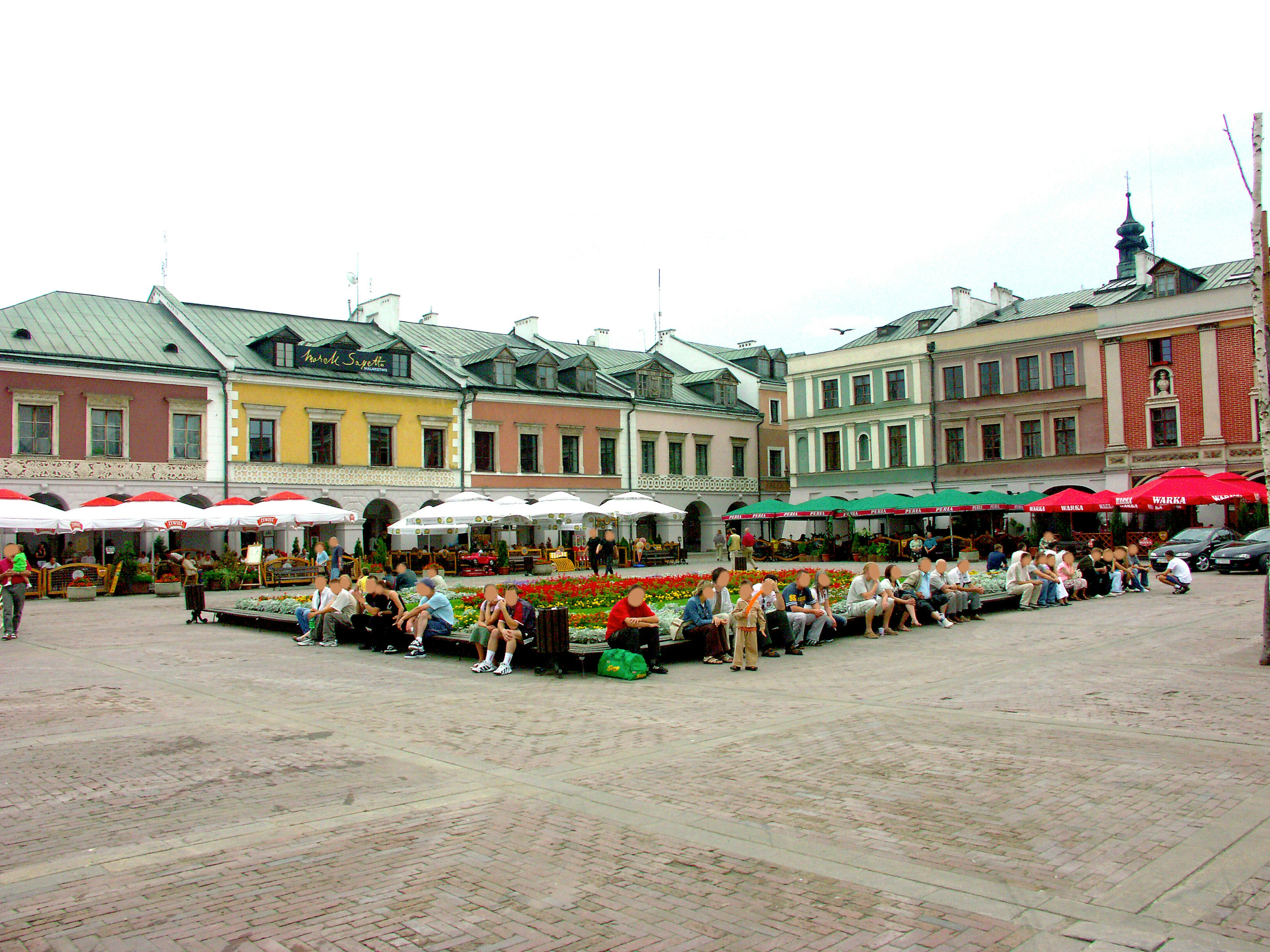 A vibrant square with people gathered colorful buildings and umbrellas