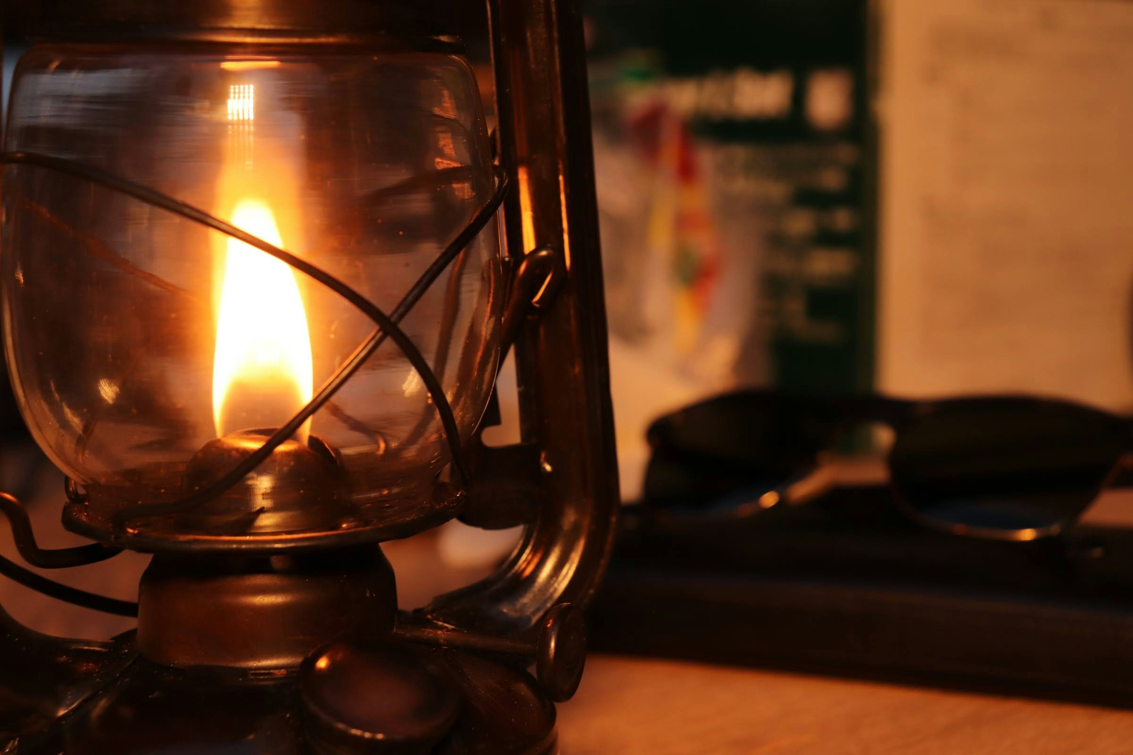 An oil lantern emitting warm light in the foreground with colorful materials and sunglasses in the background