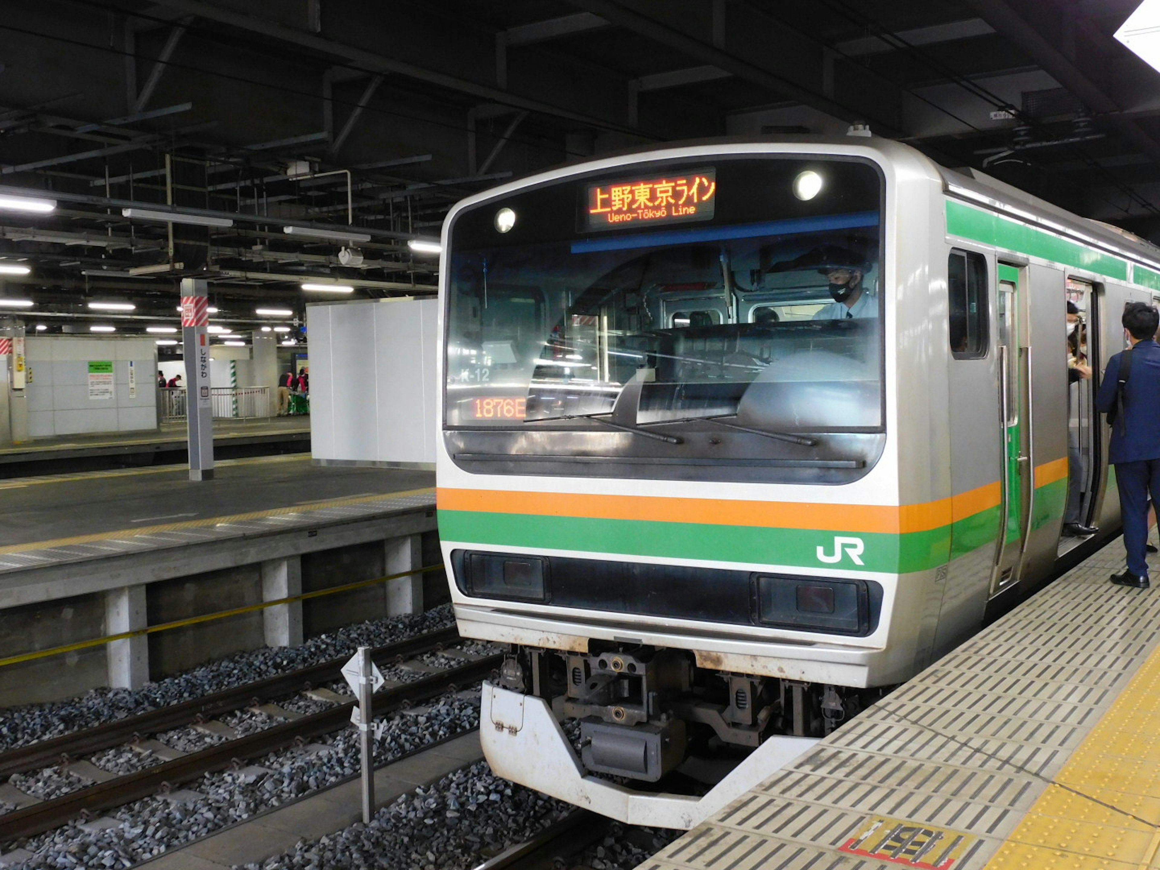 A JR train stopped at a station featuring green and orange stripes