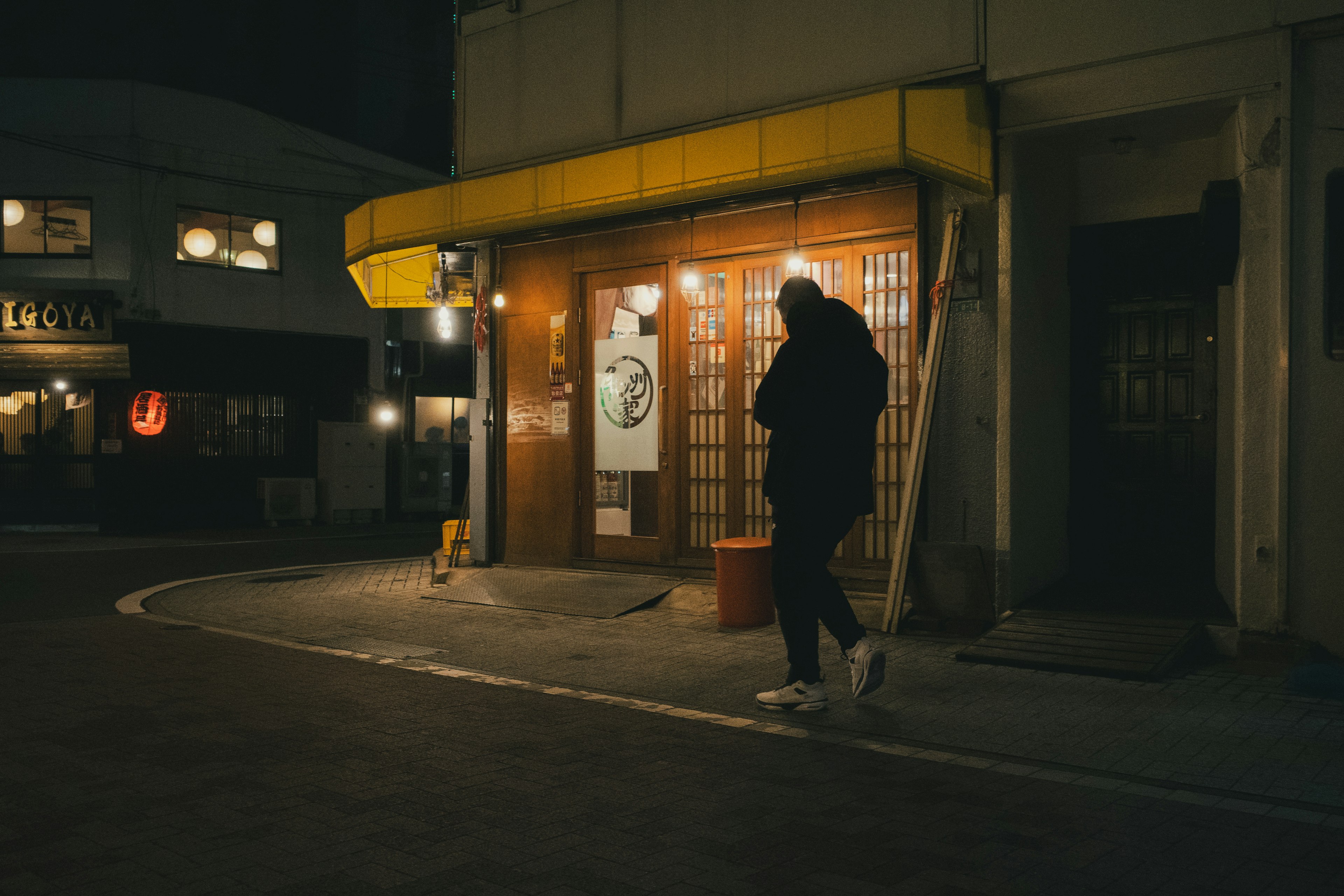 薄暗い通りを歩く人と黄色い看板の店