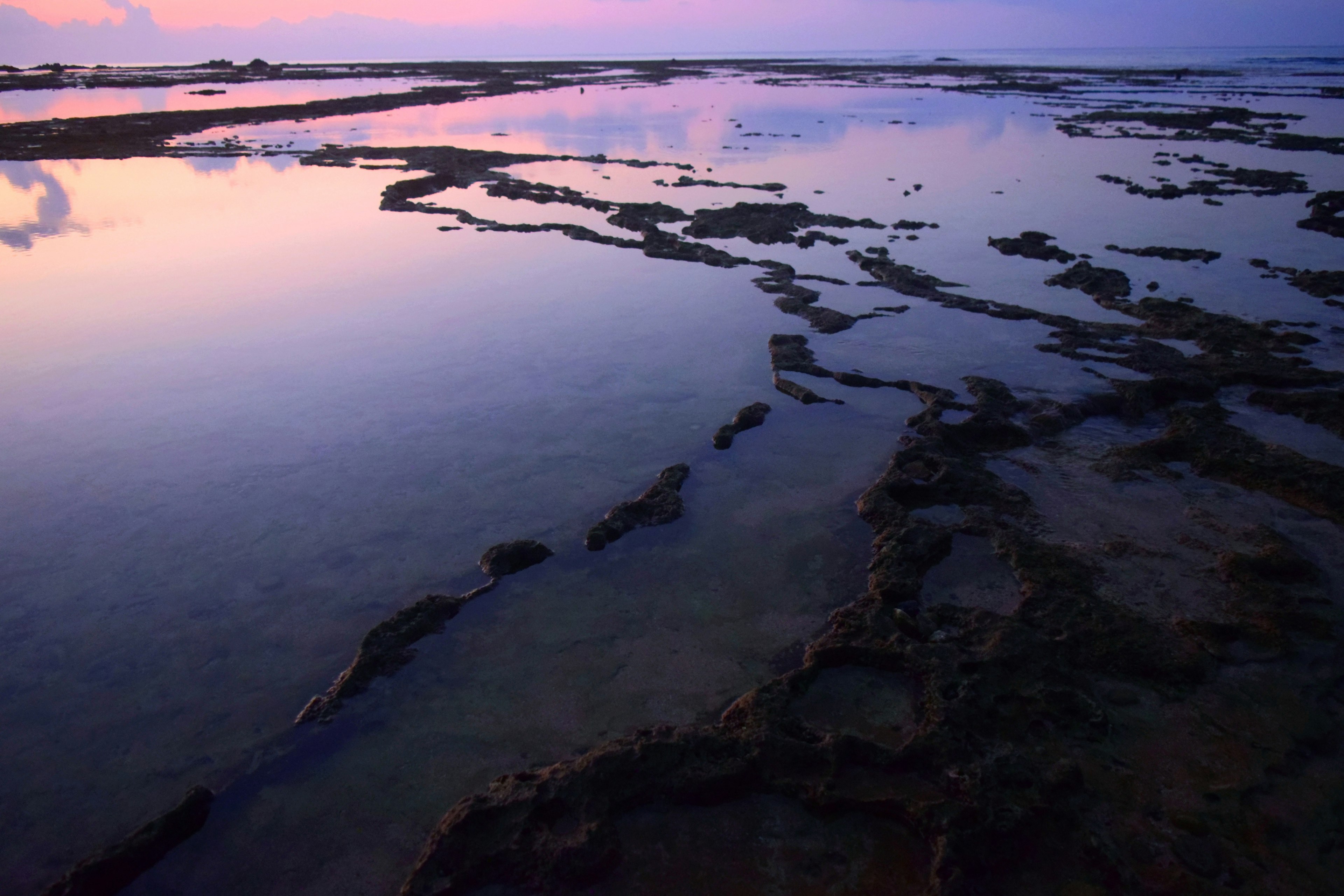 Surface d'eau calme reflétant les couleurs du crépuscule le long d'une côte rocheuse