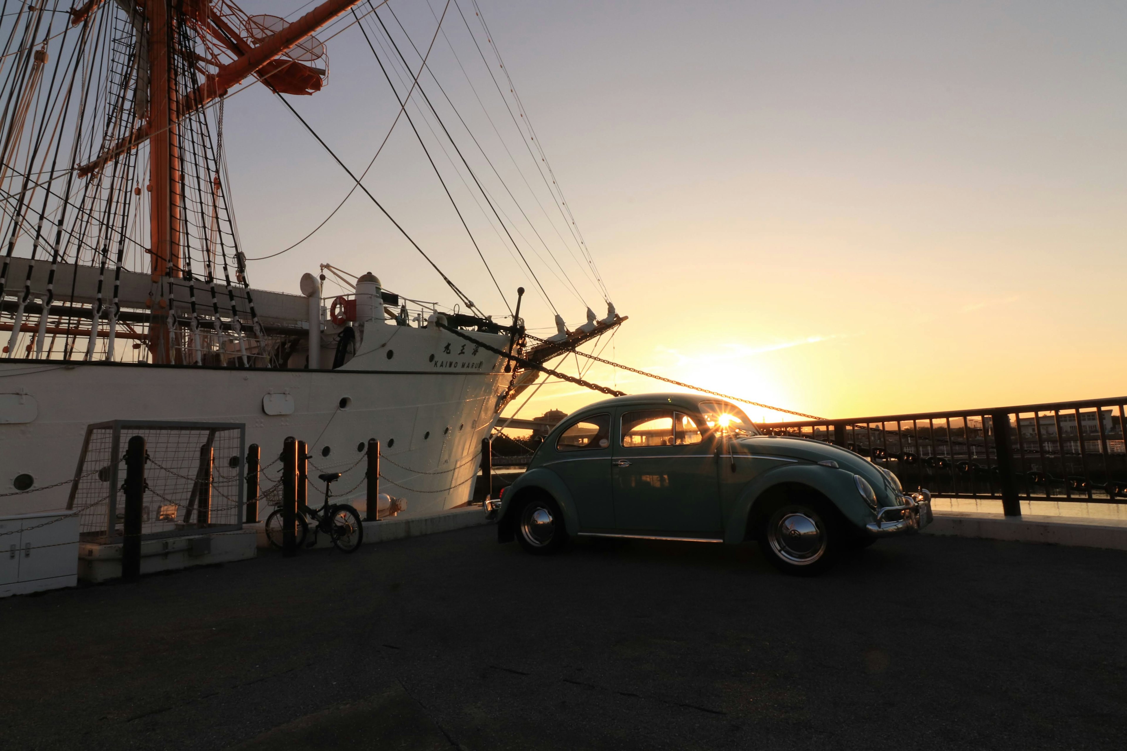 Blue Beetle car with a large sailing ship at sunset