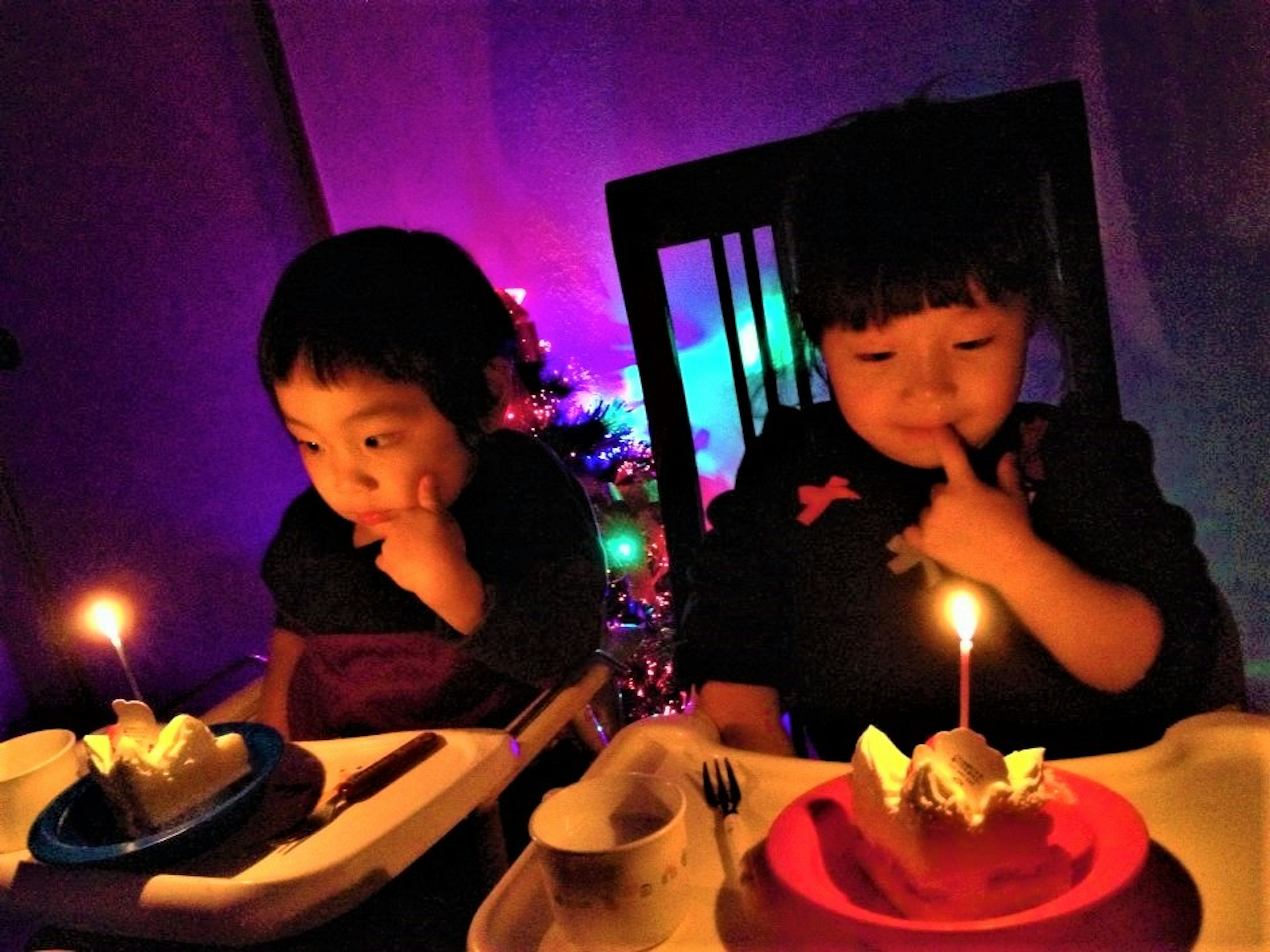 Dua anak duduk dengan kue ulang tahun dan lilin di latar belakang berwarna-warni