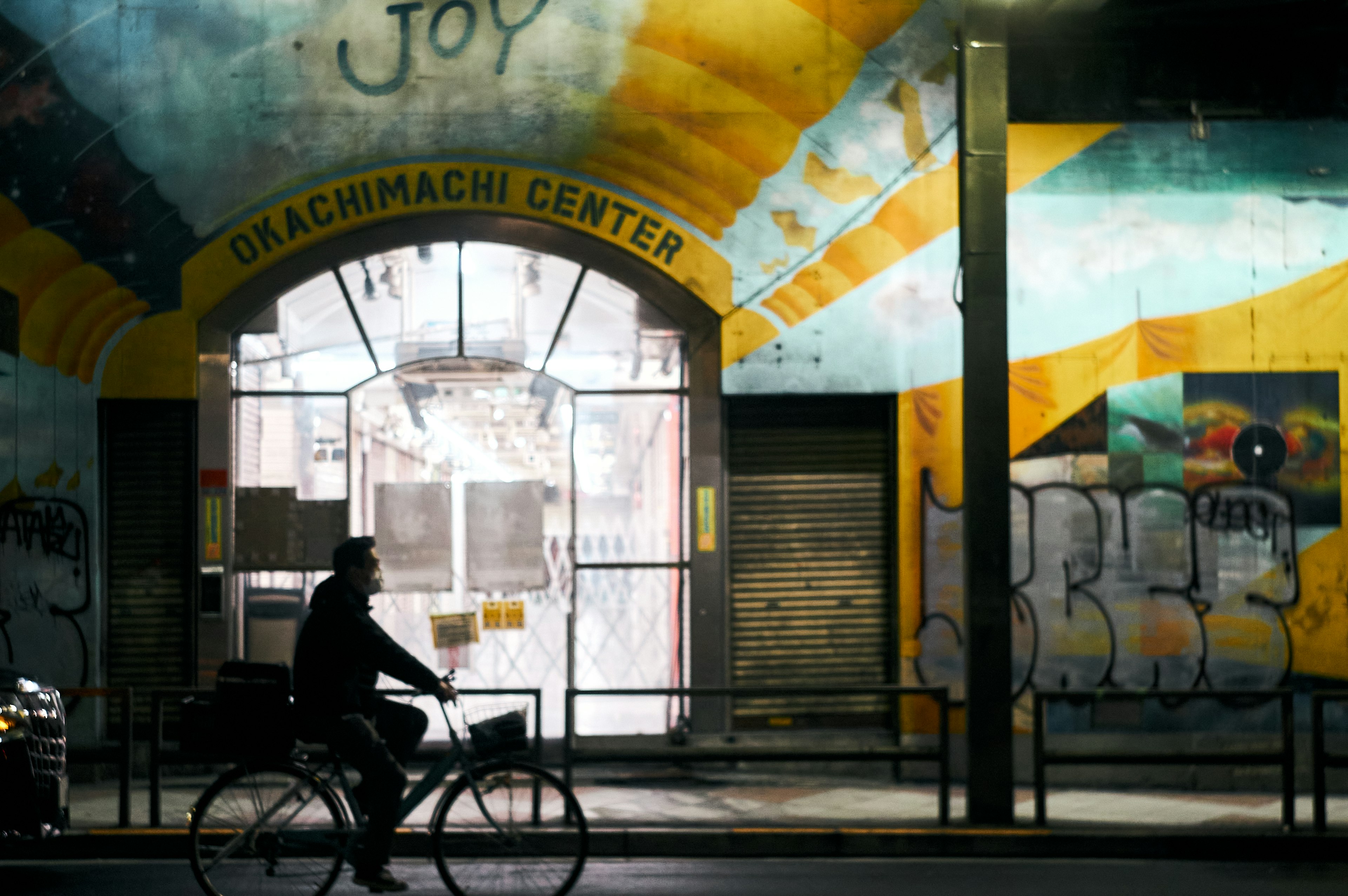 Ciclista in silhouette che passa sotto un murale colorato al Giacchiamachi Center