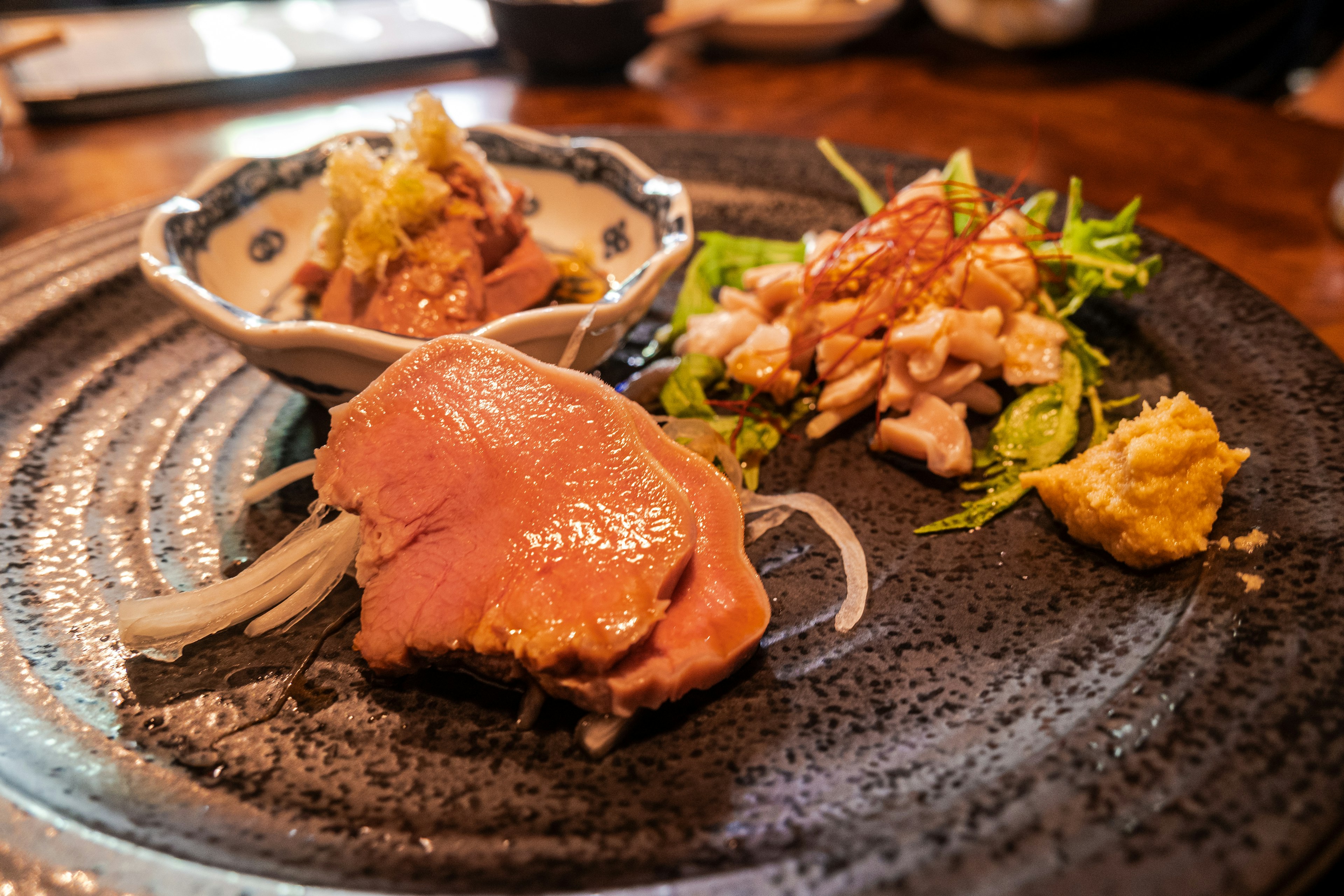 Plat de viande tranchée servi sur une assiette noire texturée avec de la salade