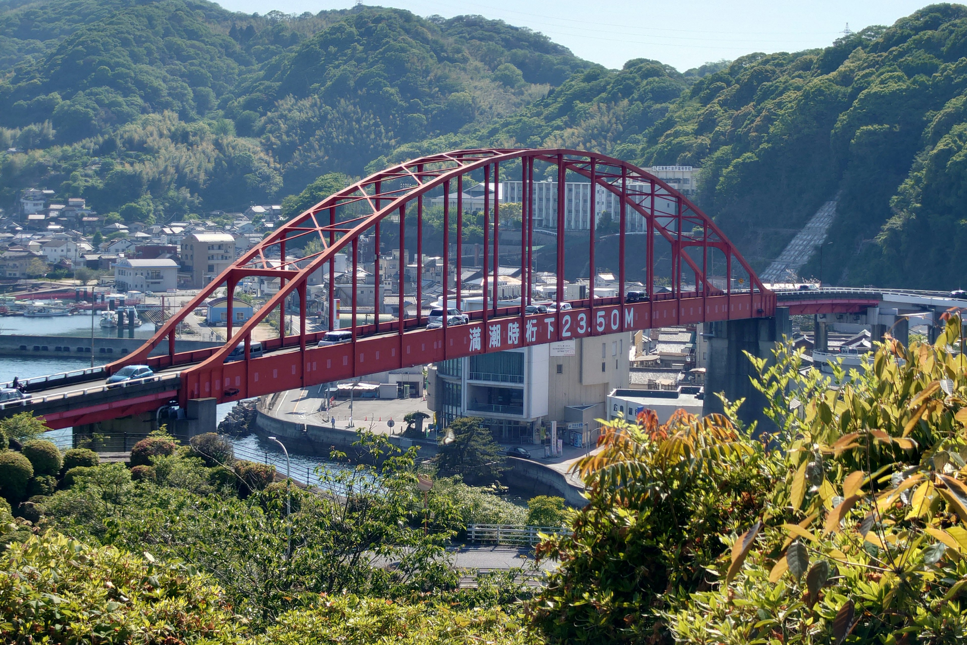 红色拱桥横跨河流，背景是绿色山丘和小镇