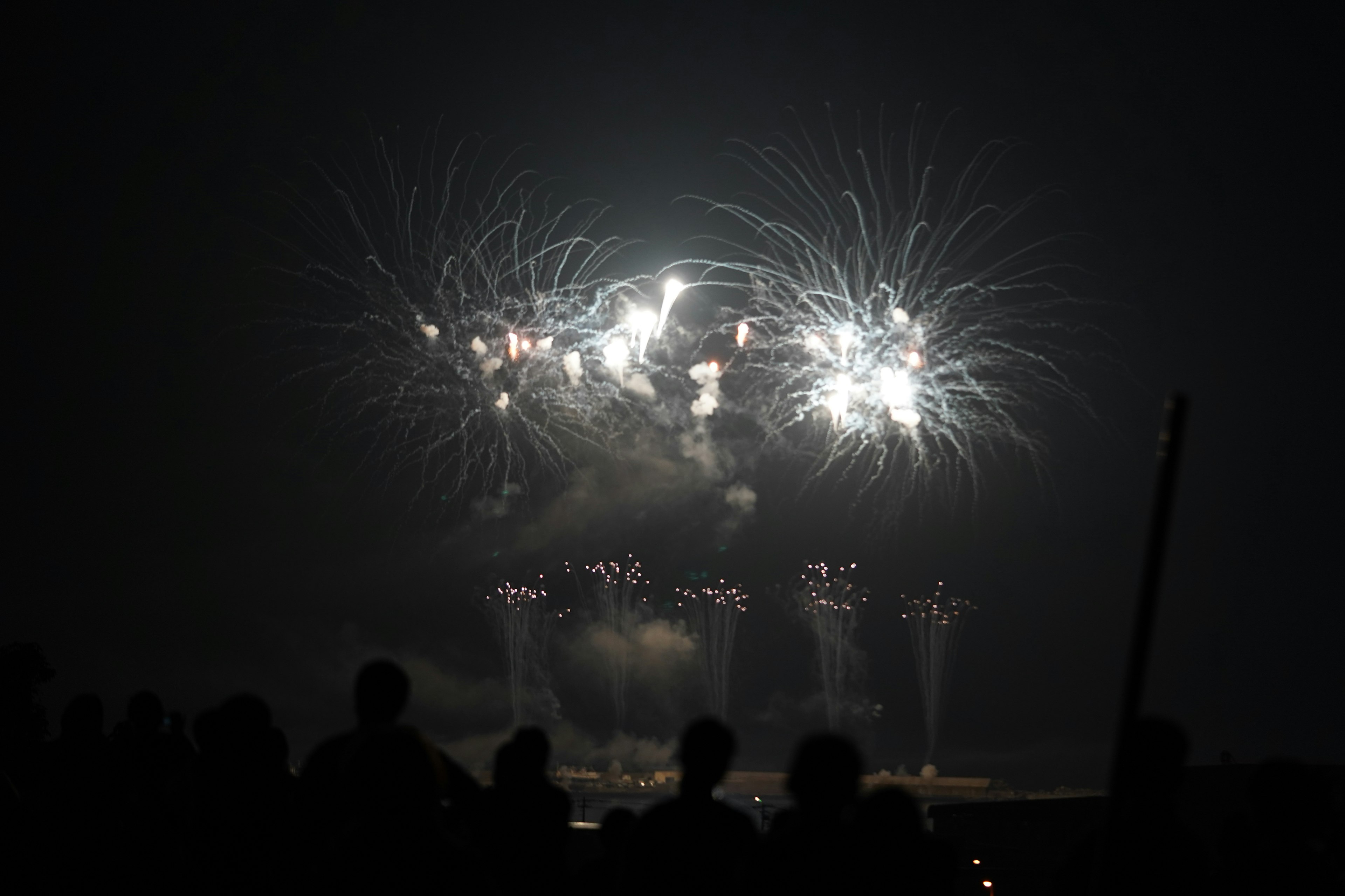 Spektakuläre Feuerwerkshow, die den Nachthimmel mit Silhouetten von Zuschauern beleuchtet