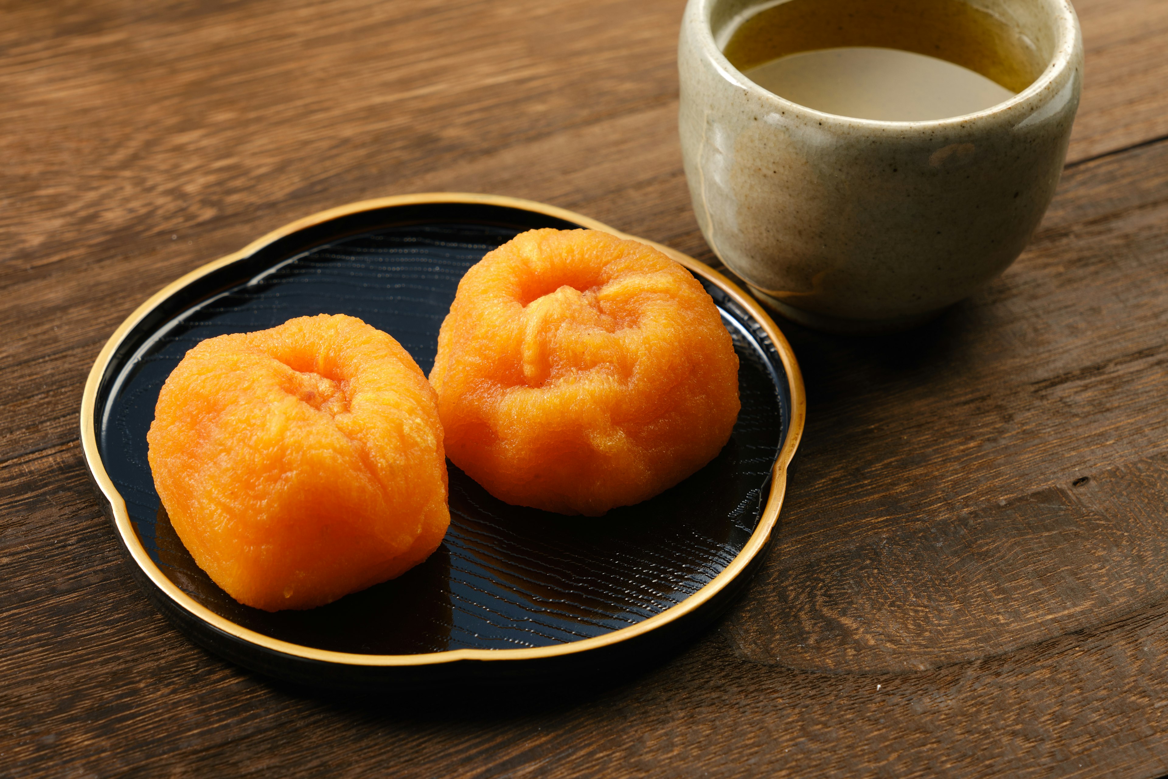 Two orange Japanese sweets on a black plate beside a tea cup