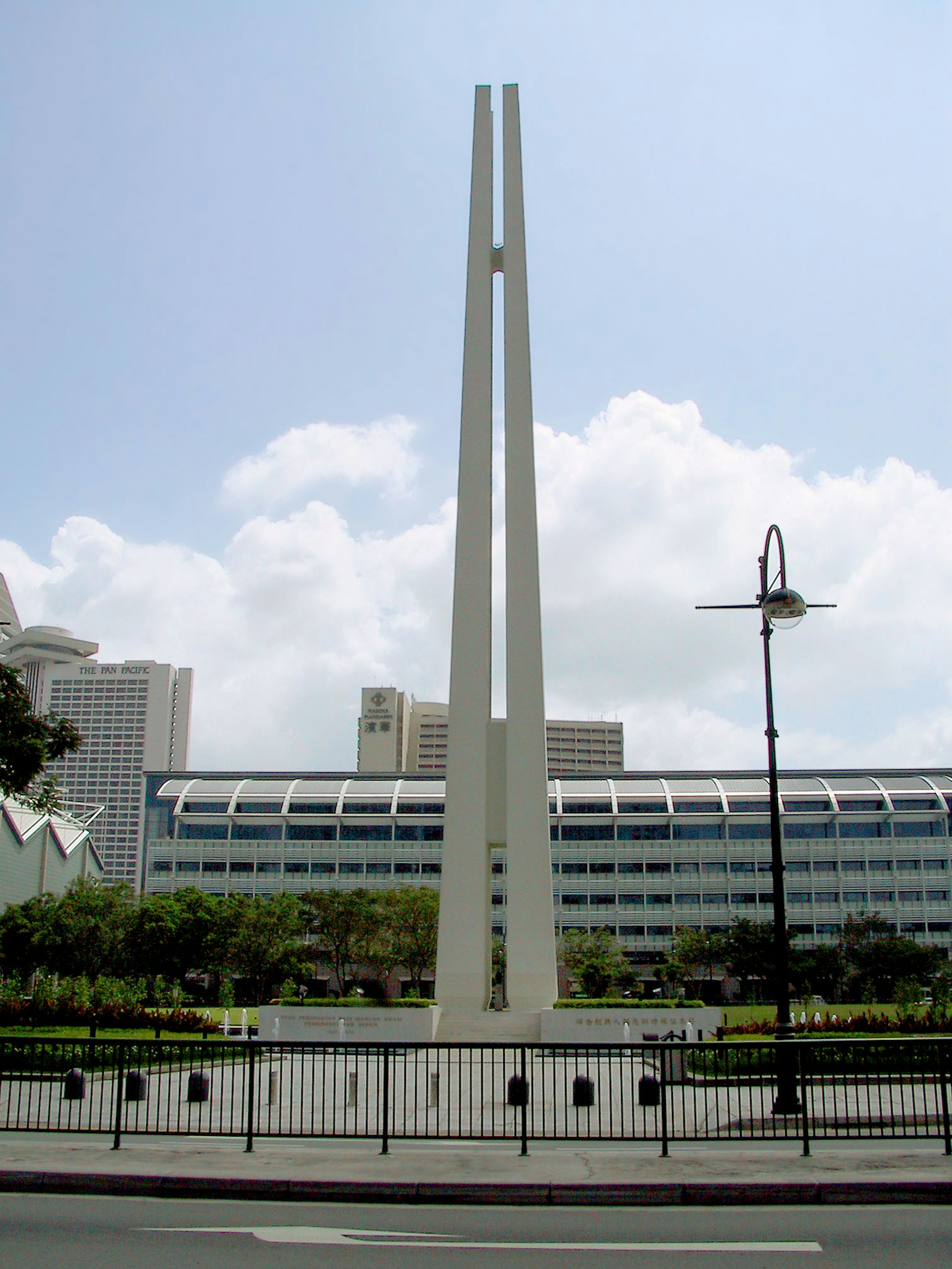 Photo of a monument in Singapore featuring tall white spires surrounded by green grass and modern buildings