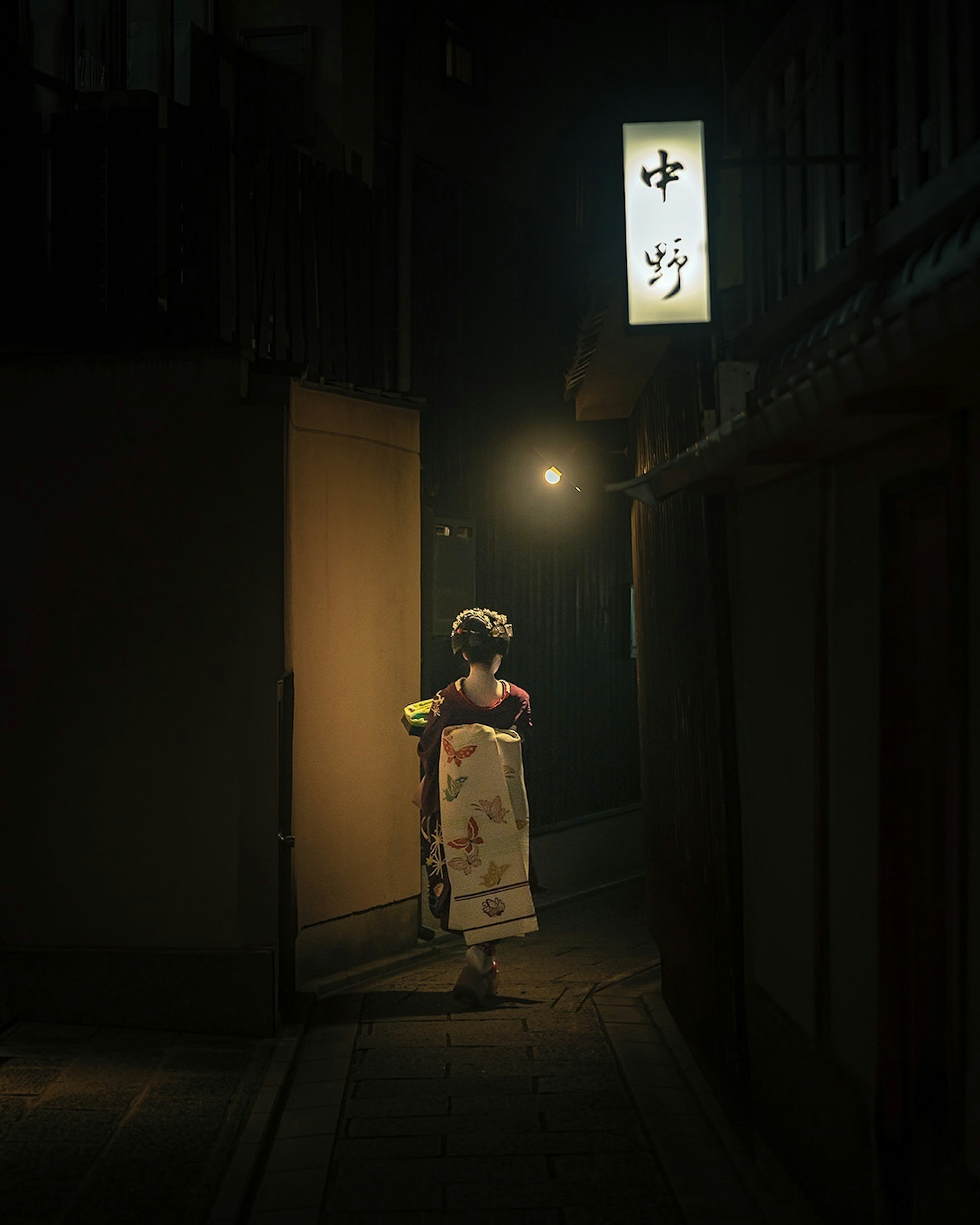 Eine Frau im Kimono steht in einer dunklen Gasse mit einer Laterne