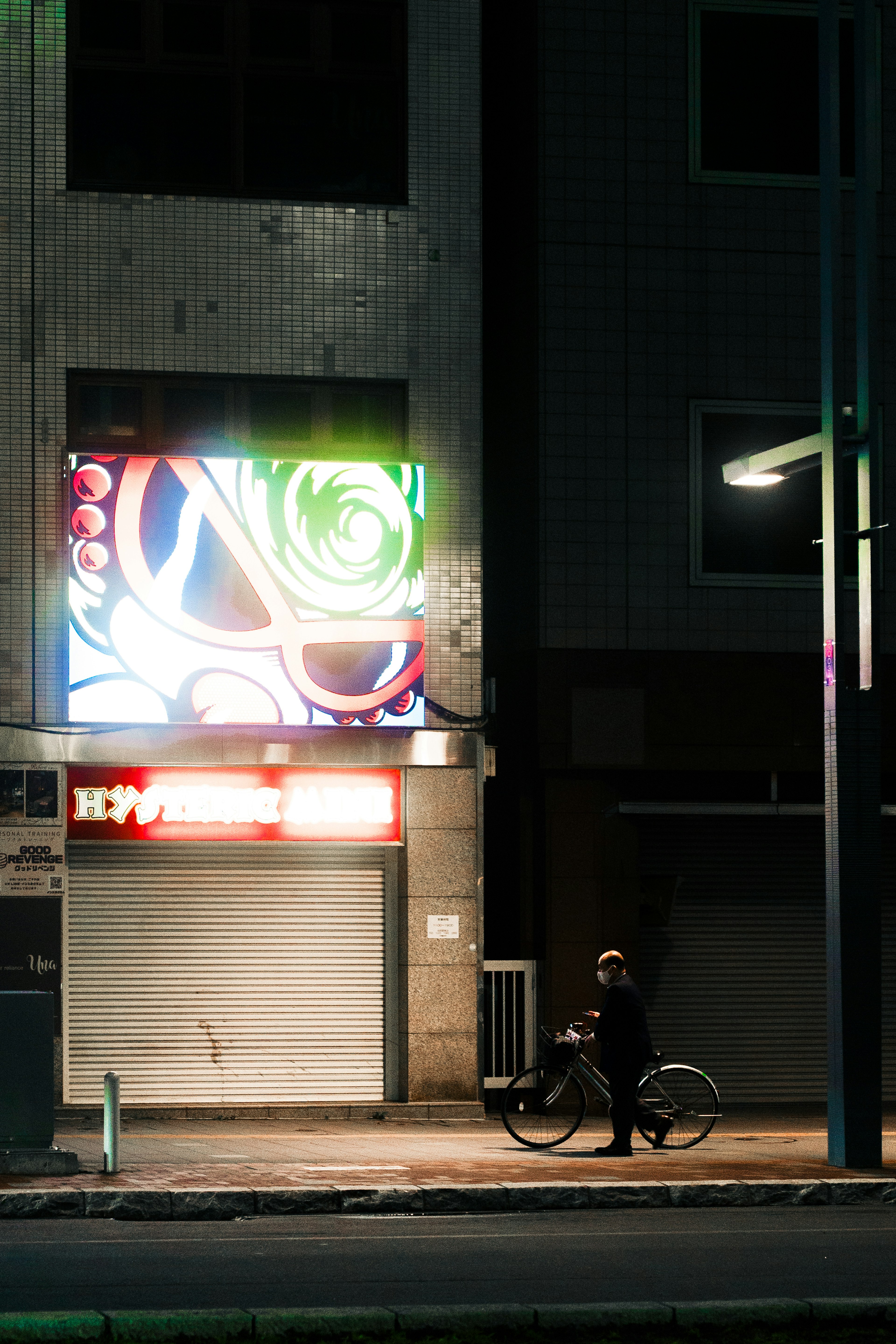 A person riding a bicycle in a city at night with a colorful sign