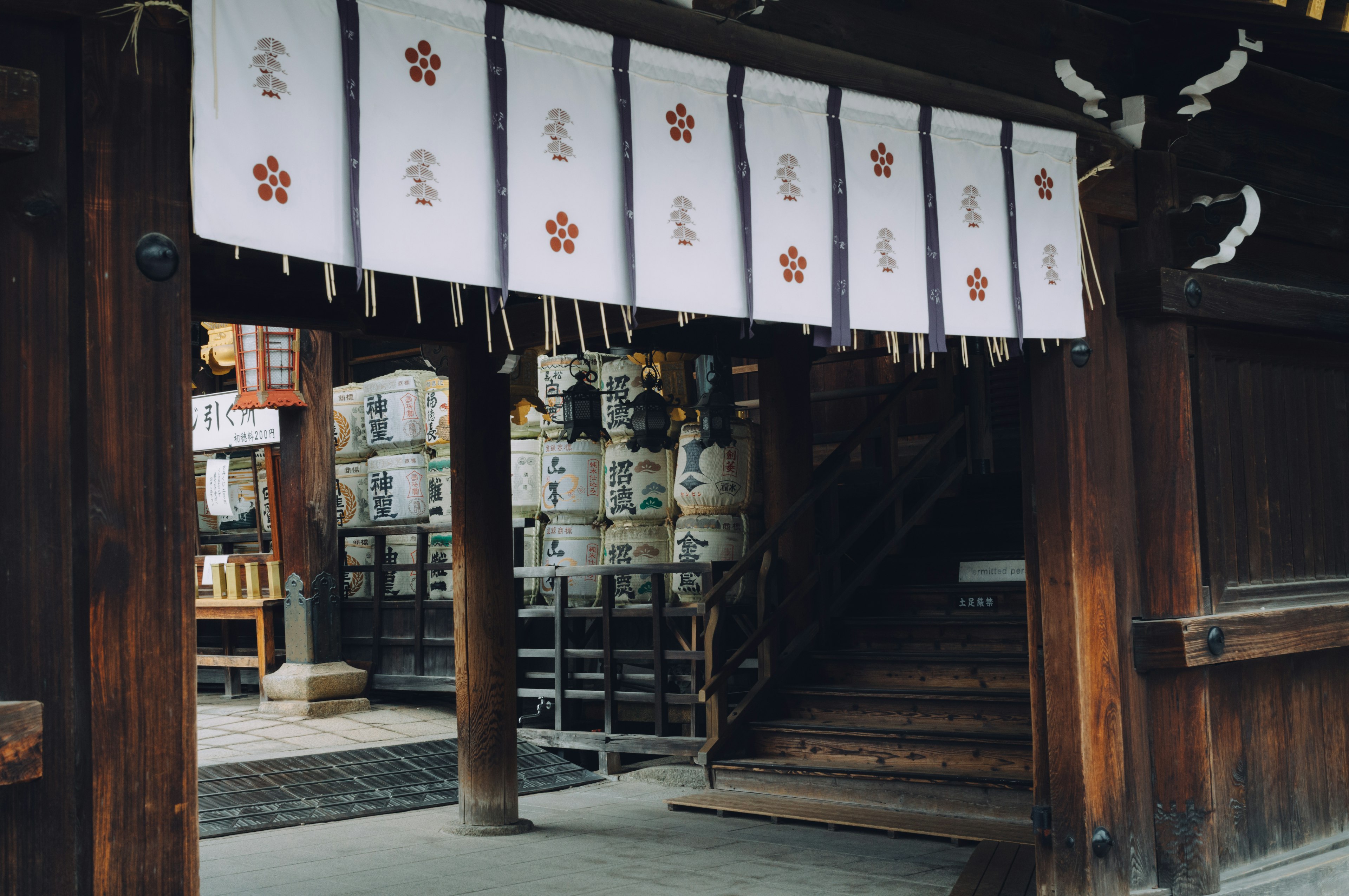 Entrance of a wooden shrine with hanging white curtains and sake barrels