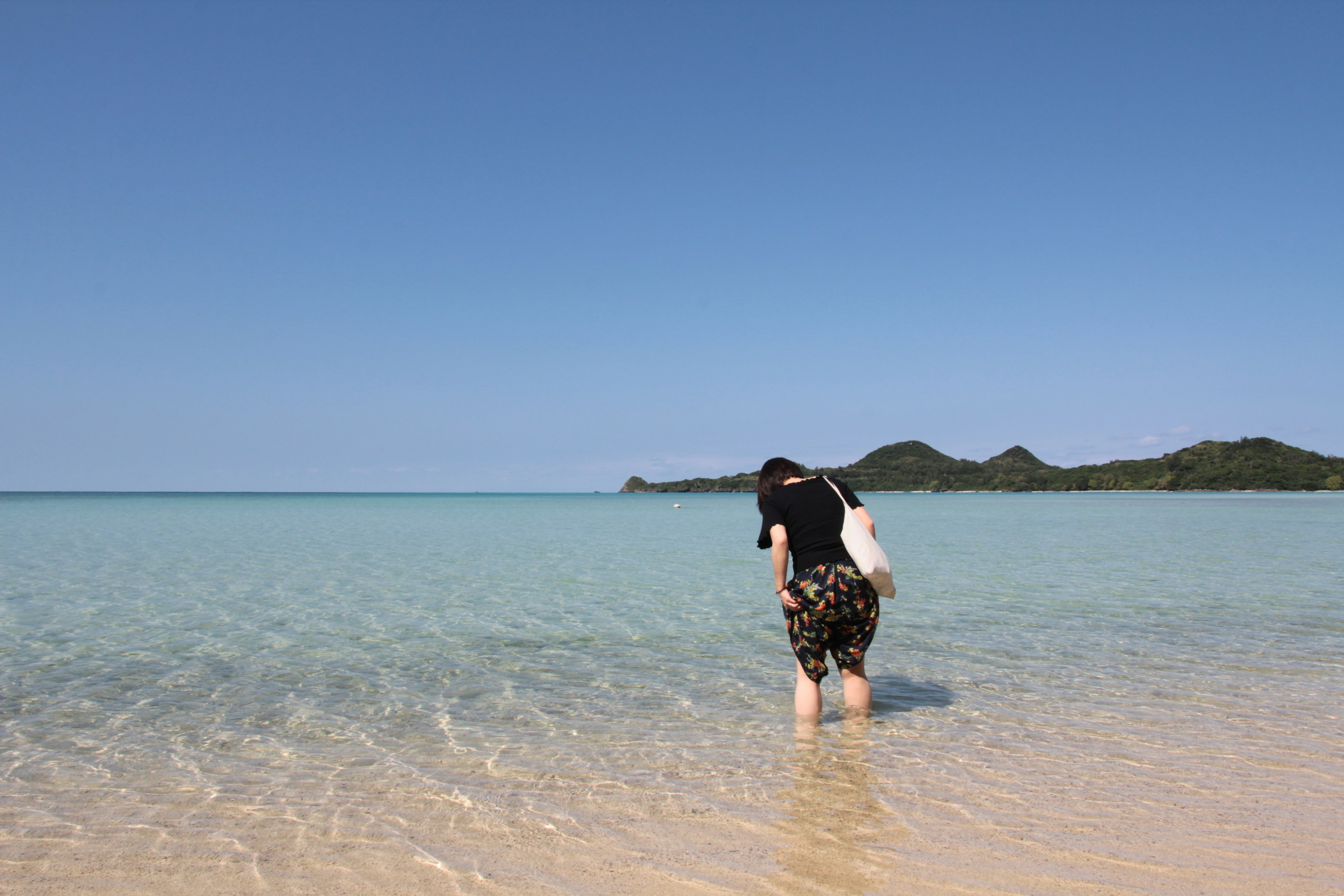 青い海と白い砂浜を背景にした人が水に足を浸している