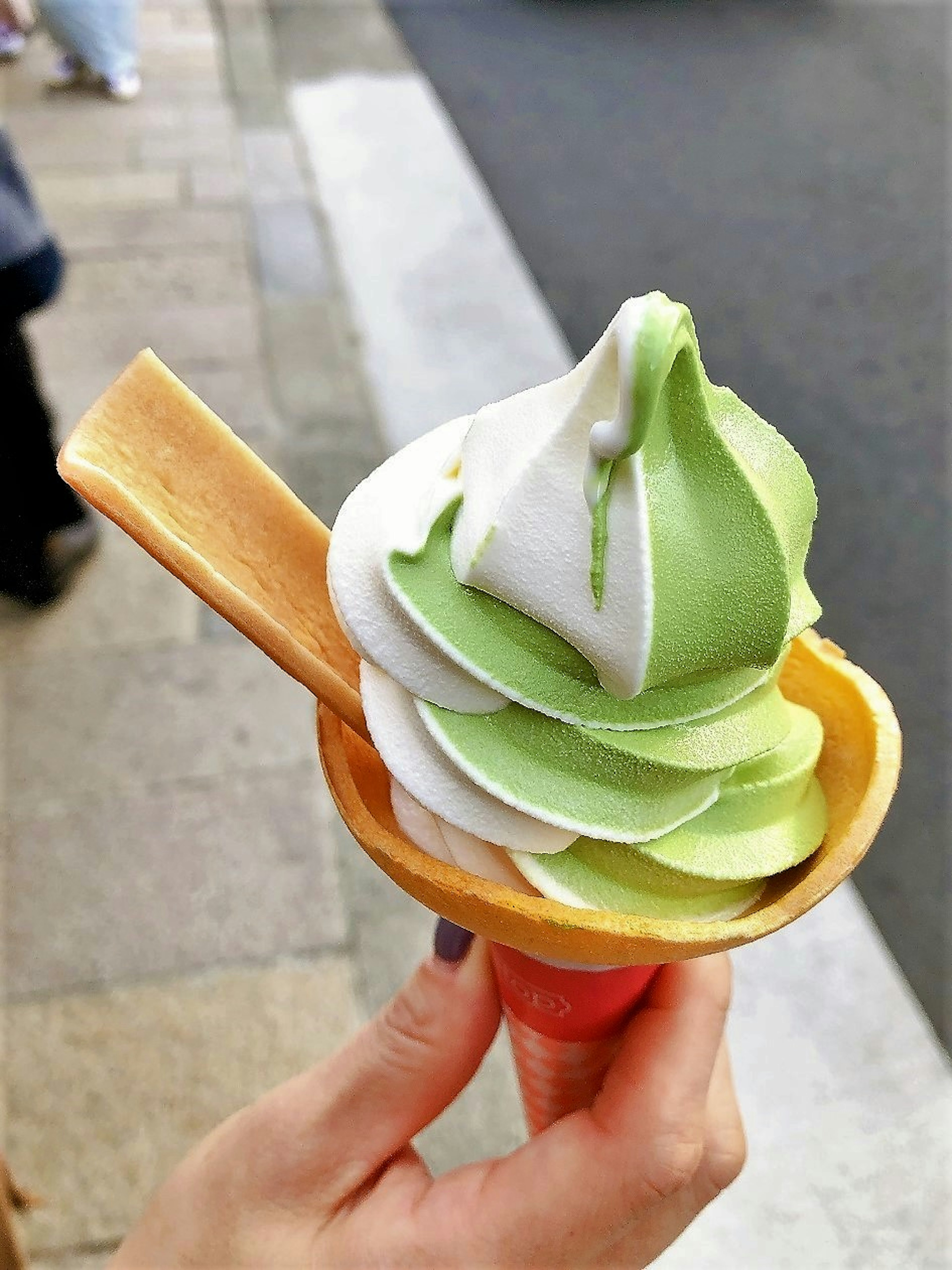 Una mano sosteniendo un cono de helado suave de matcha y vainilla