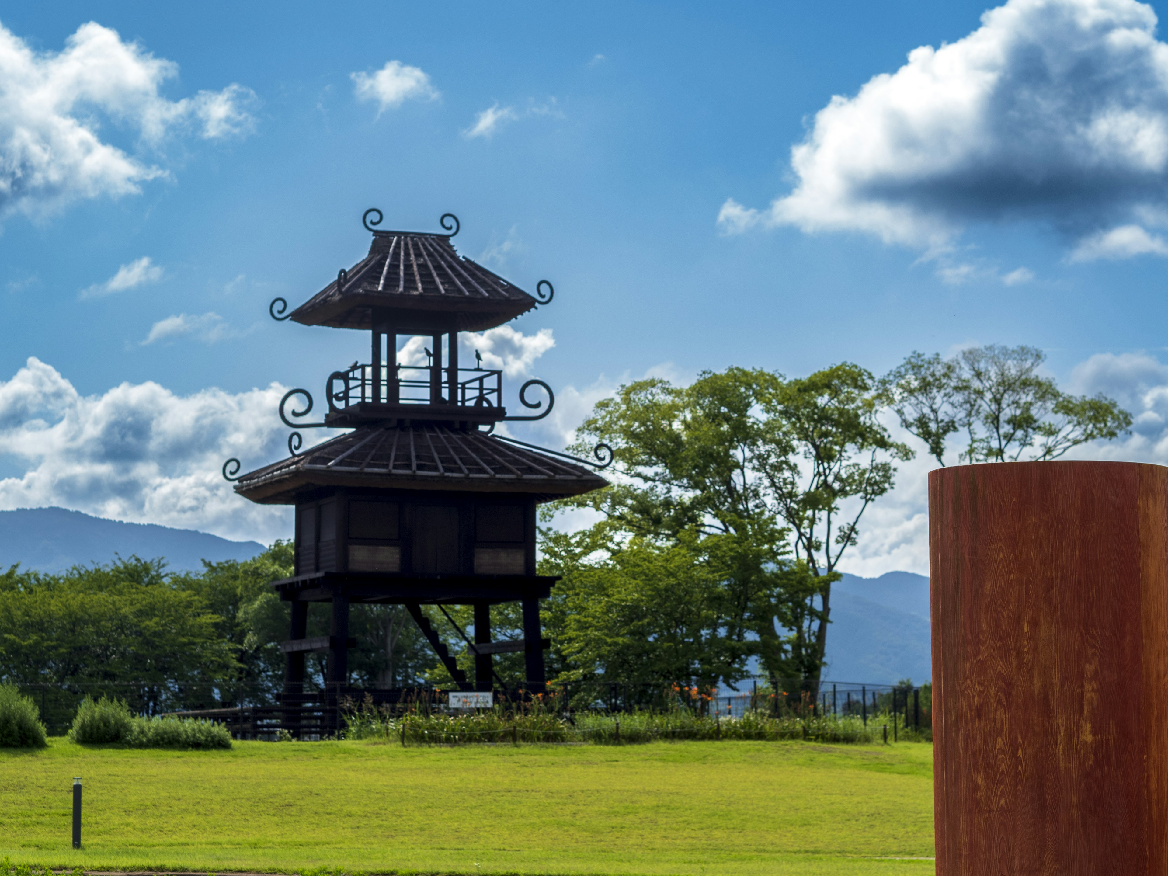 Traditional Japanese tower under a blue sky with greenery