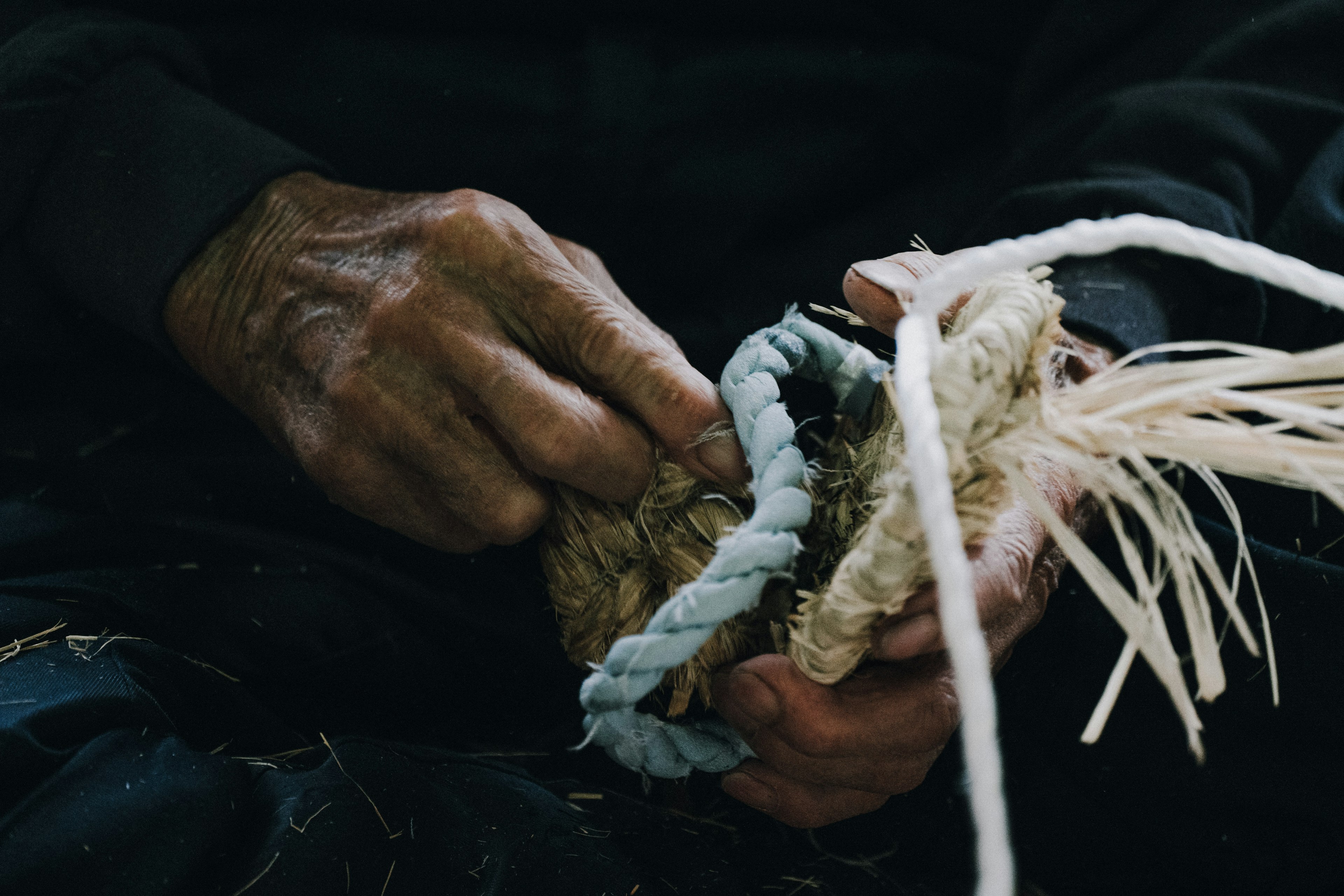 Manos de un anciano tejiendo con materiales naturales