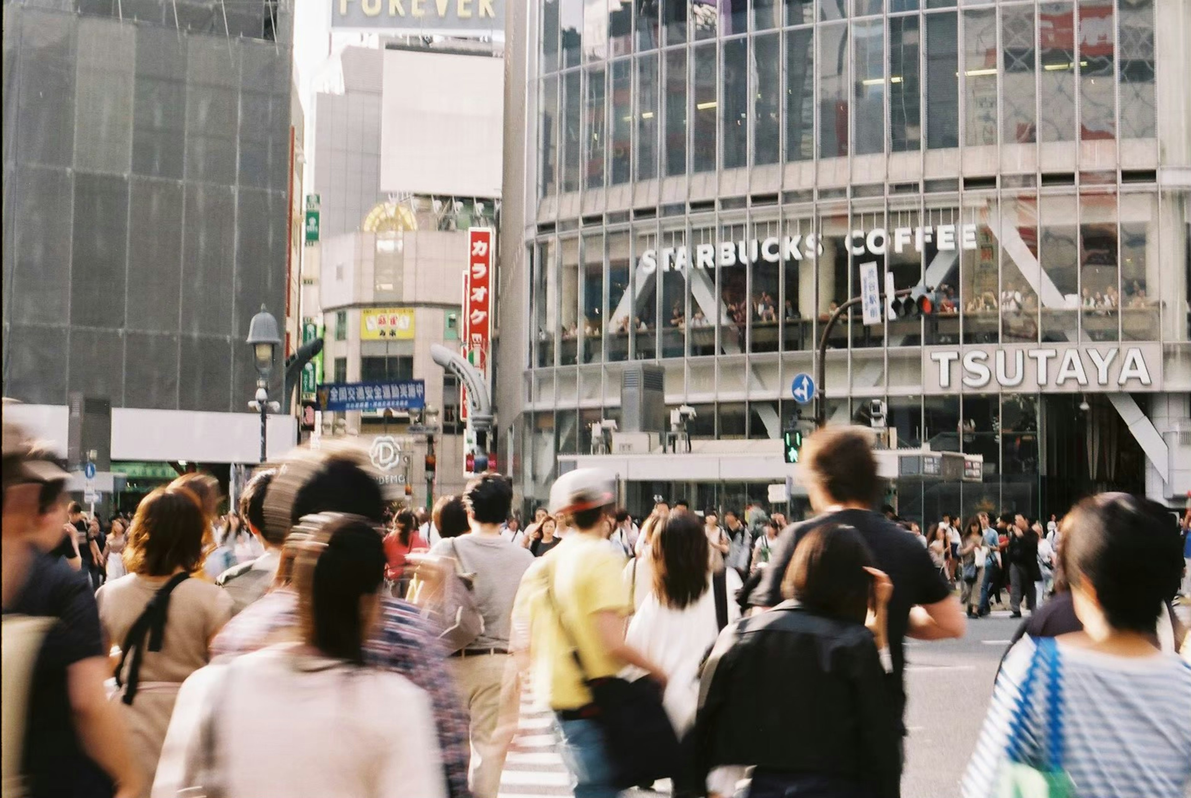 Kerumunan orang menyeberangi persimpangan Shibuya dengan Starbucks Coffee dan TSUTAYA di dekatnya