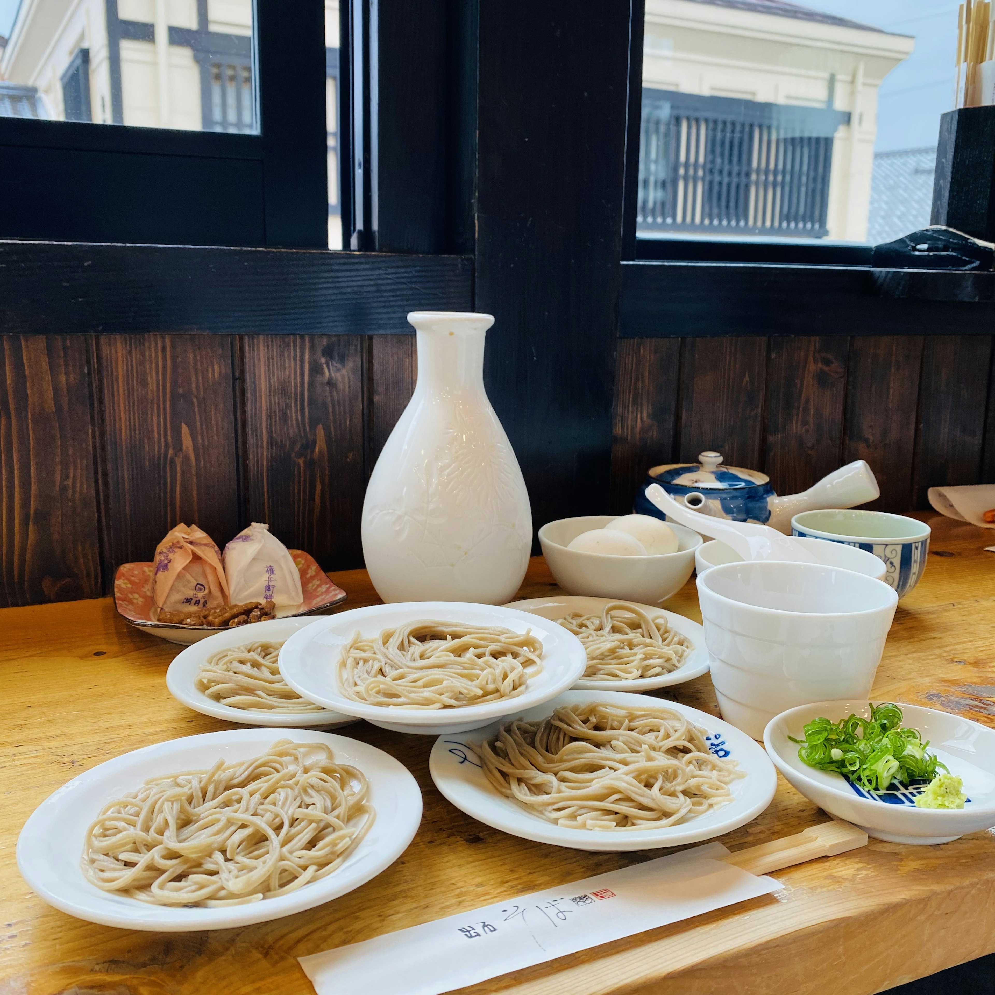 A scene featuring plates of soba noodles and green onions on a wooden table