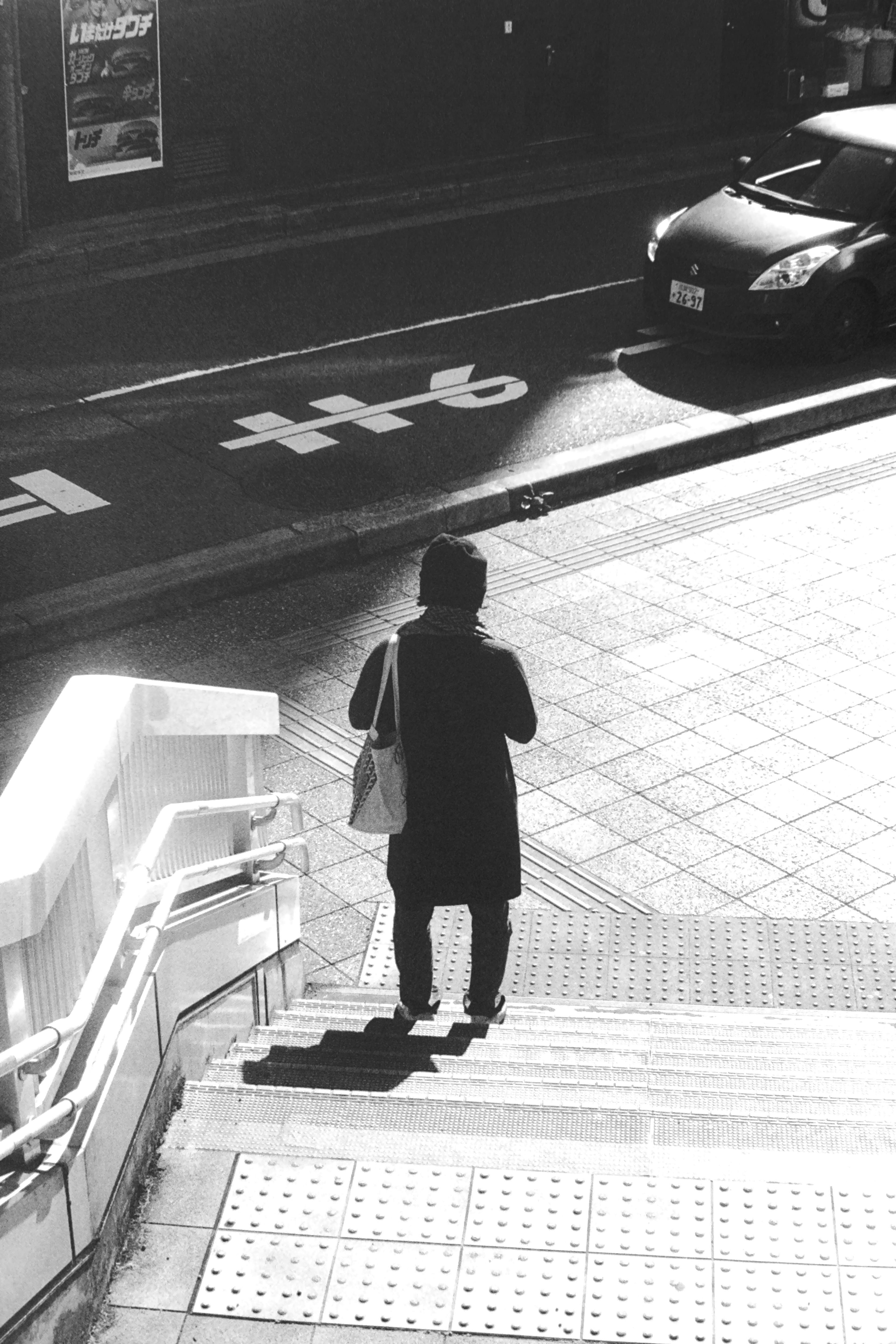 Escena de calle en blanco y negro con una persona bajando escaleras y un coche