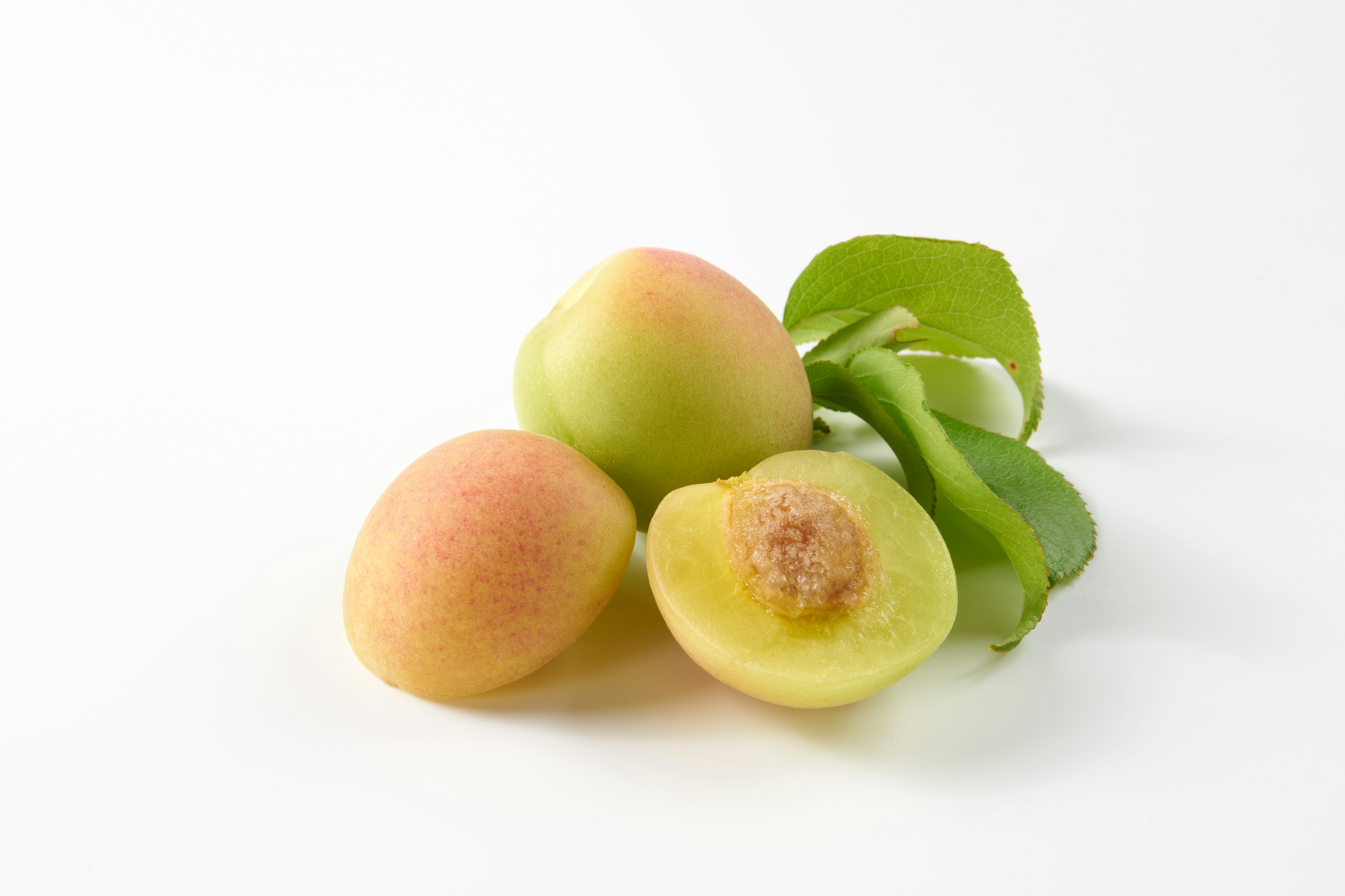 Tres frutas verdes con una rebanada y hojas sobre fondo blanco