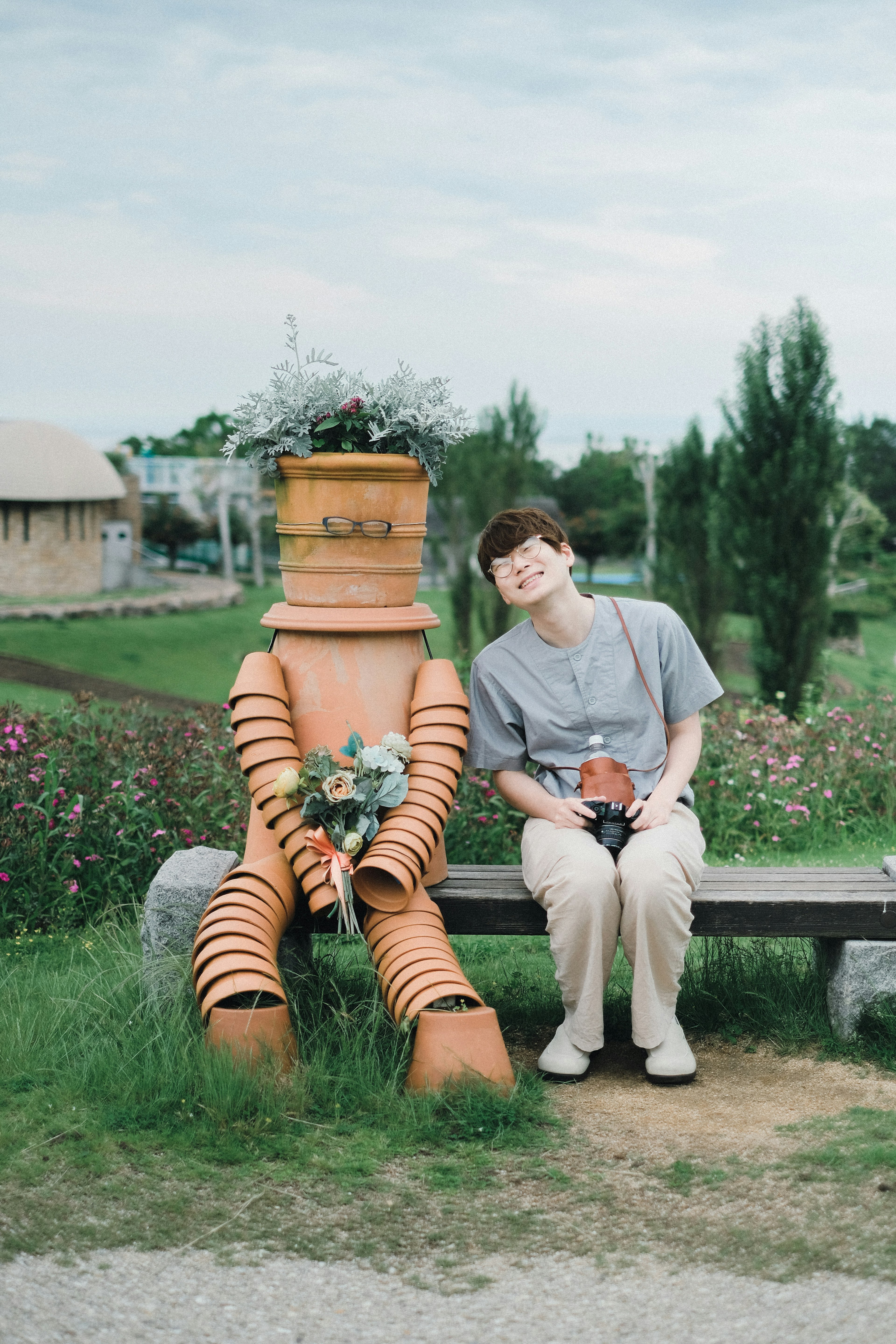 A young person sitting on a bench next to a flower-holding robot made of plant pots