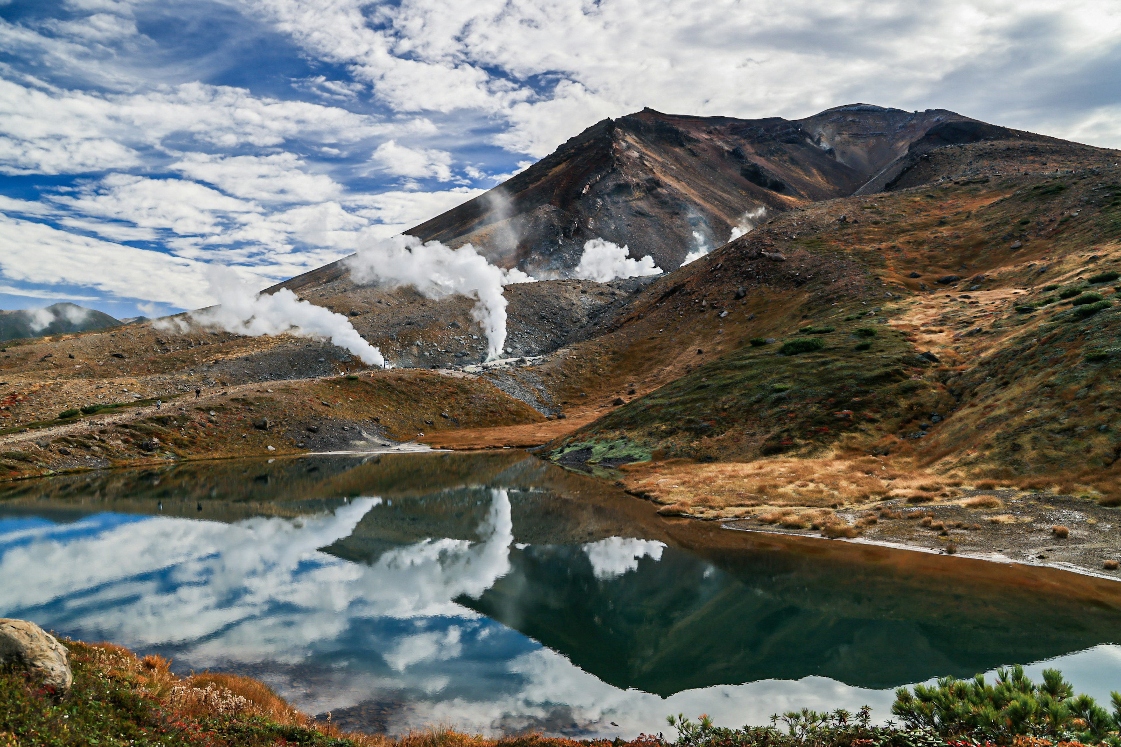 雲のある空の下に広がる山と湖の風景 煙を上げる温泉が見える